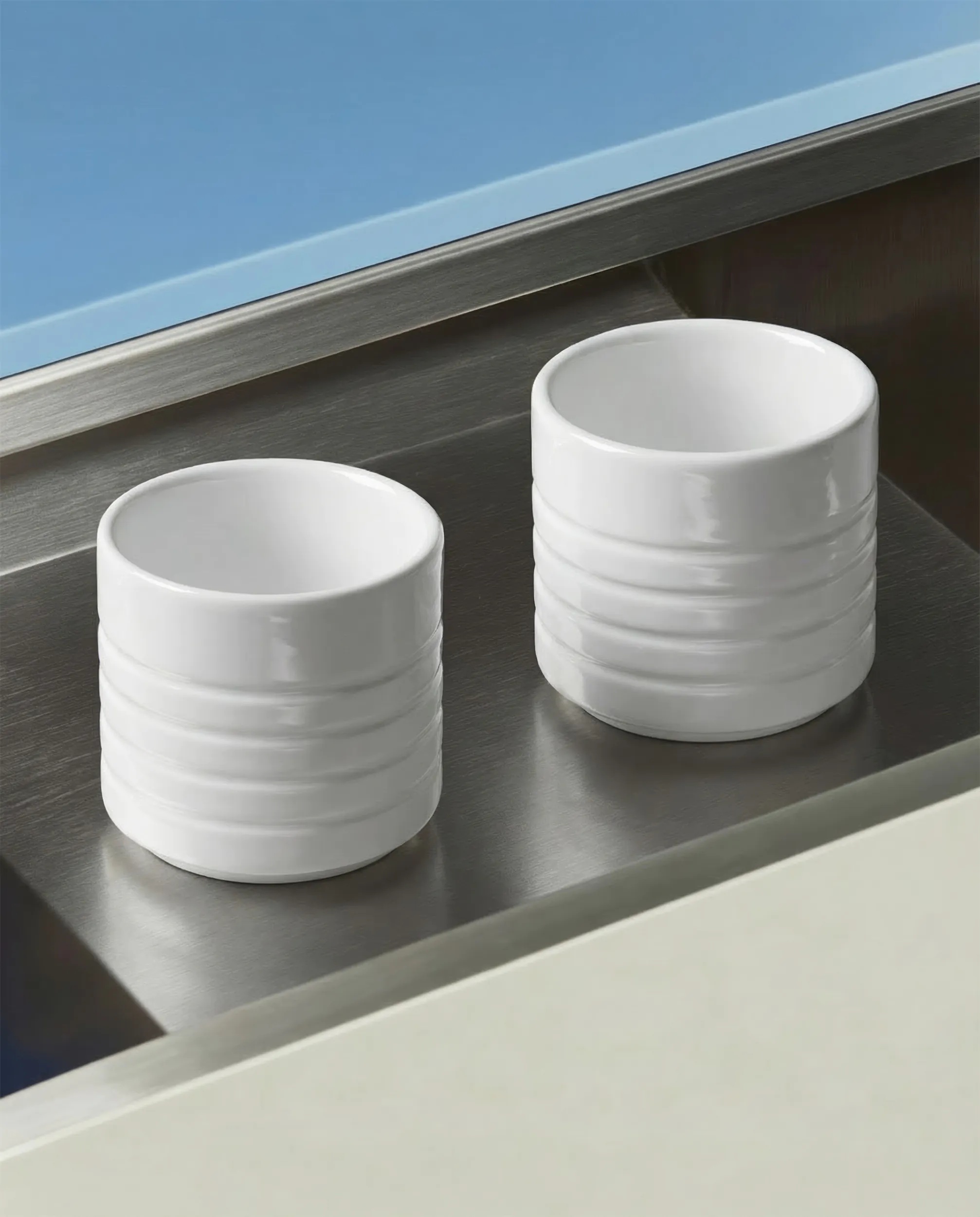 Два белых цилиндрических керамических предмета на поверхности из нержавеющей стали.
