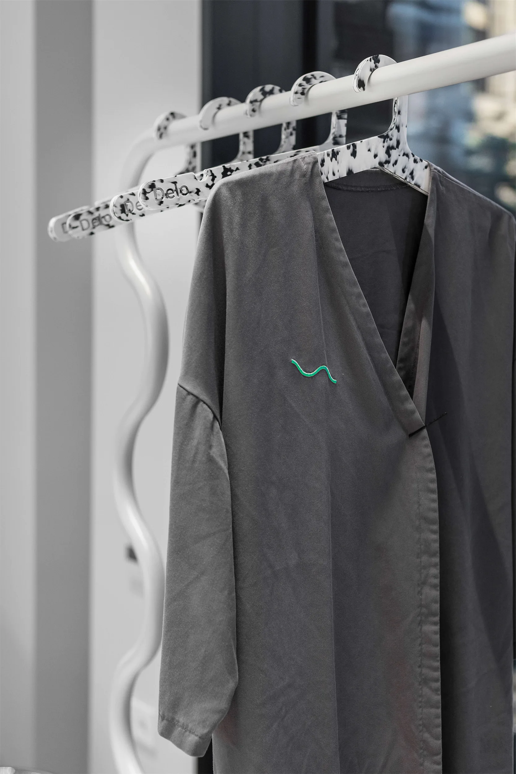 Серая рубашка с зелёным логотипом на белой пластиковой вешалке.