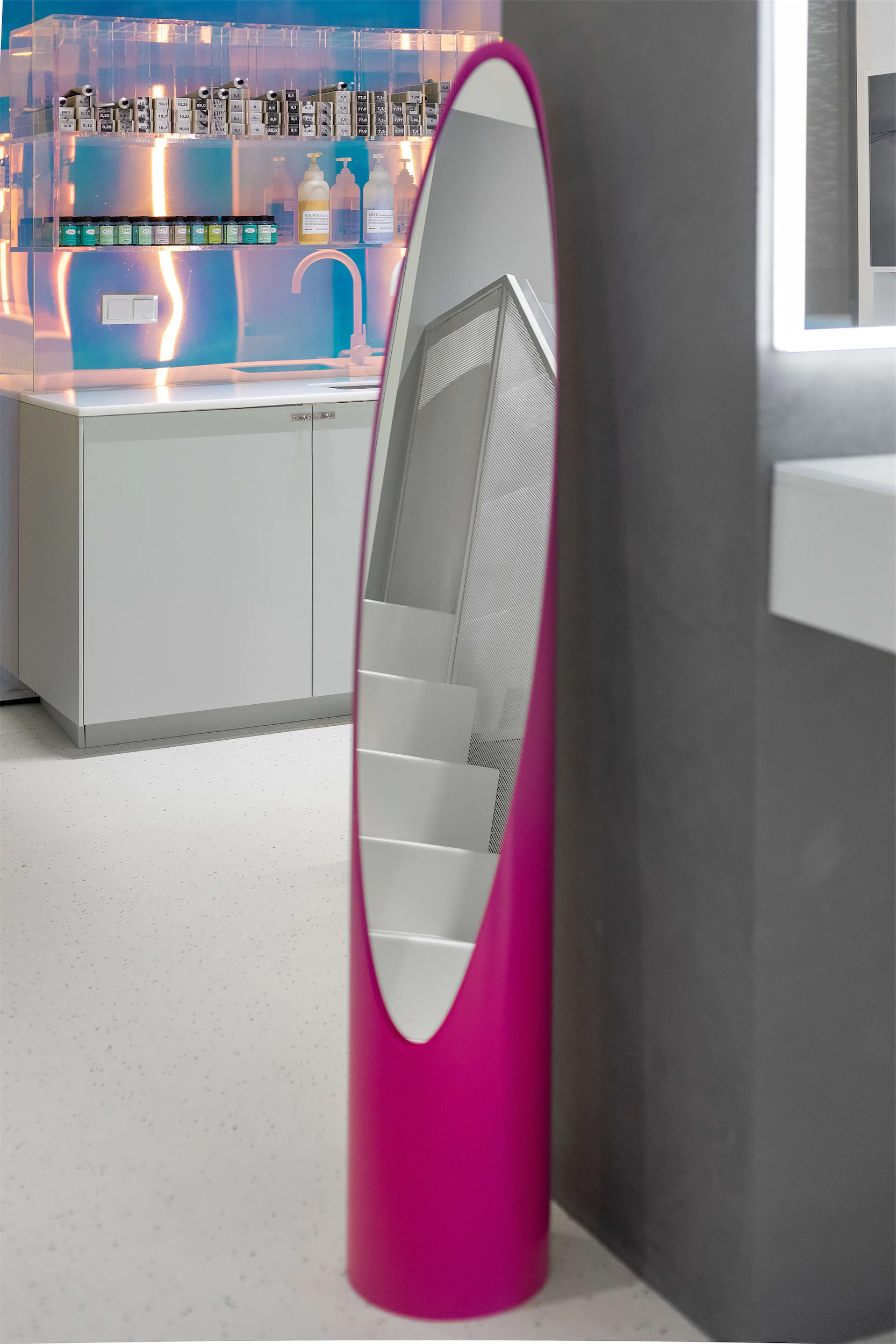 Изогнутая розовая витрина с белым внутренним пространством и полками у серой стены.