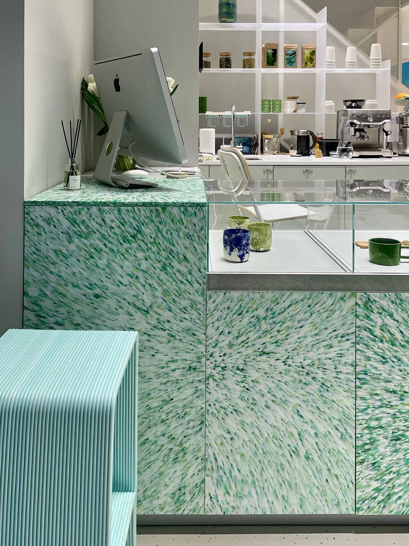 Рабочее место со столом с узором под зелёный мрамор, монитором и канцелярией.