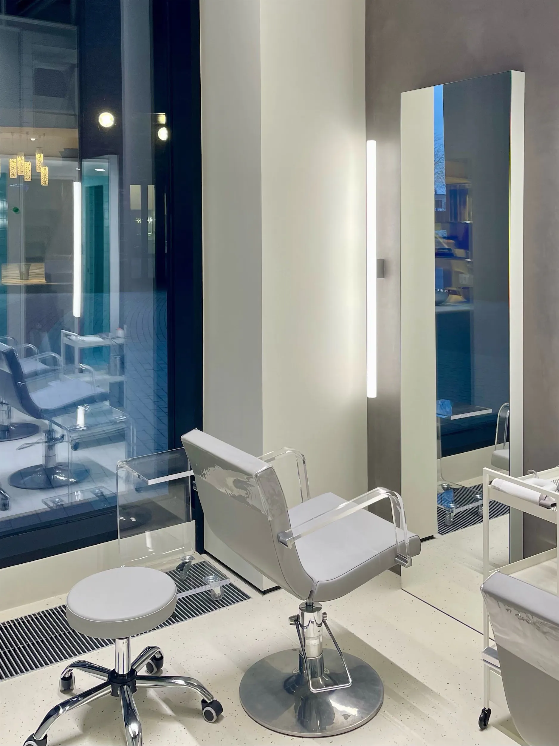Белое парикмахерское кресло перед большим зеркалом на белом полу.
