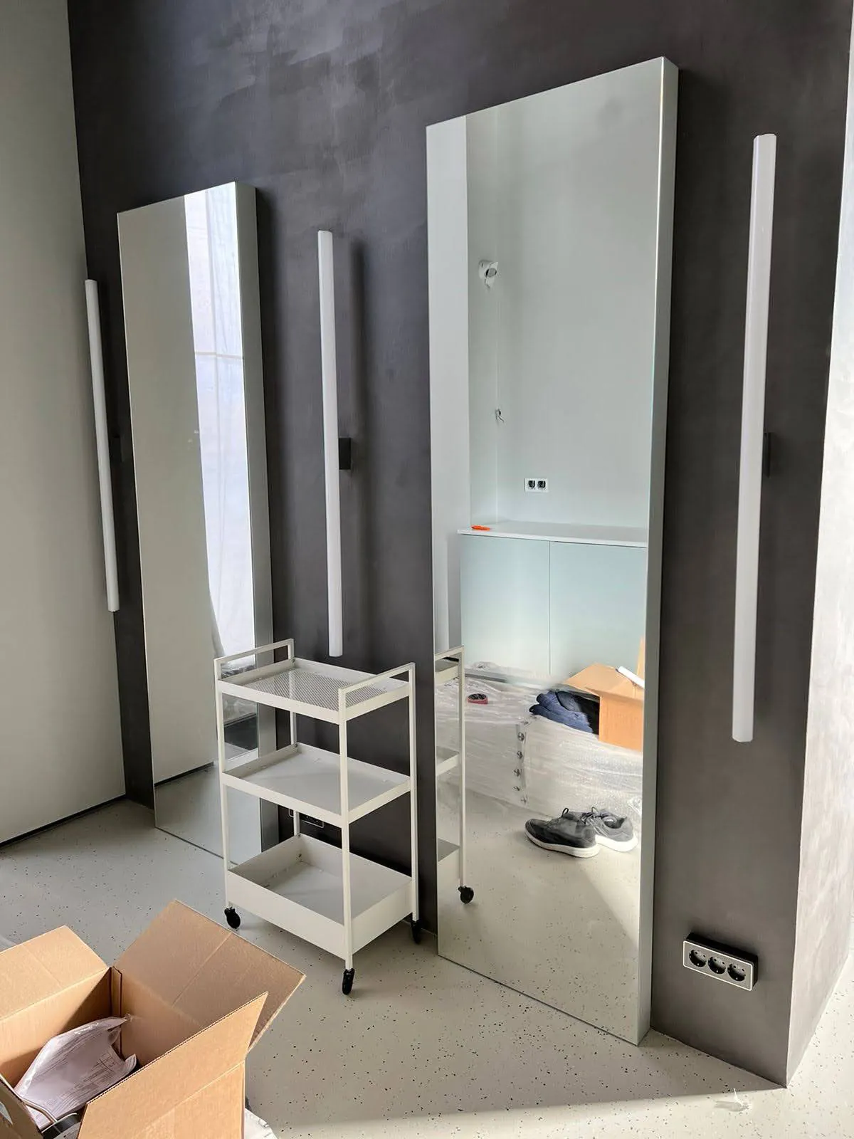 Белый стеллаж на колёсиках перед высоким зеркалом.