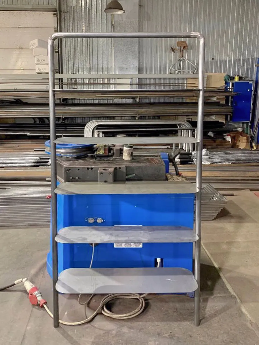 Металлический стеллаж с тремя полками и синим основанием в мастерской.