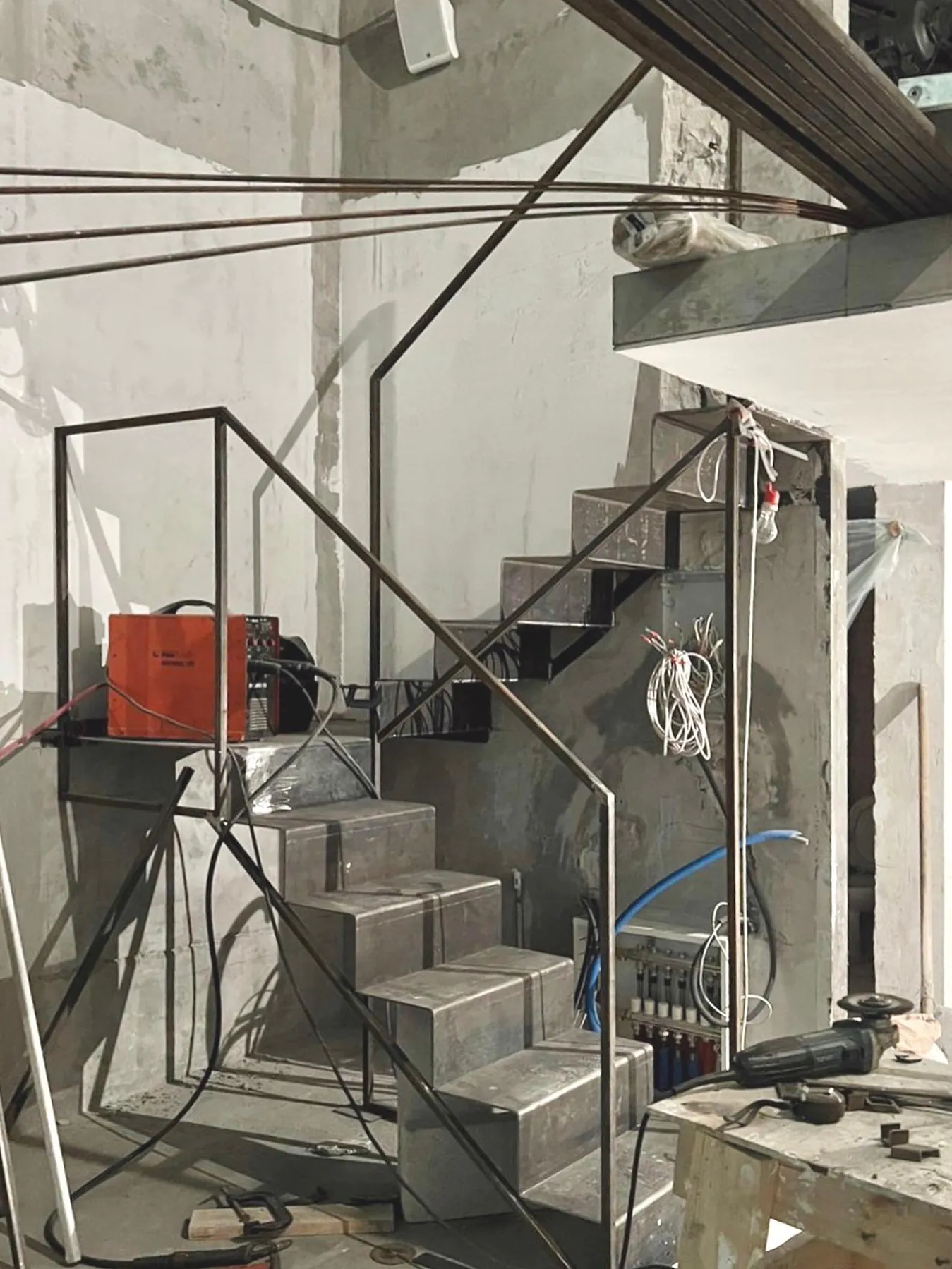 Металлическая лестница с перилами. Вдоль неё проложены кабели и стоит красный ящик.