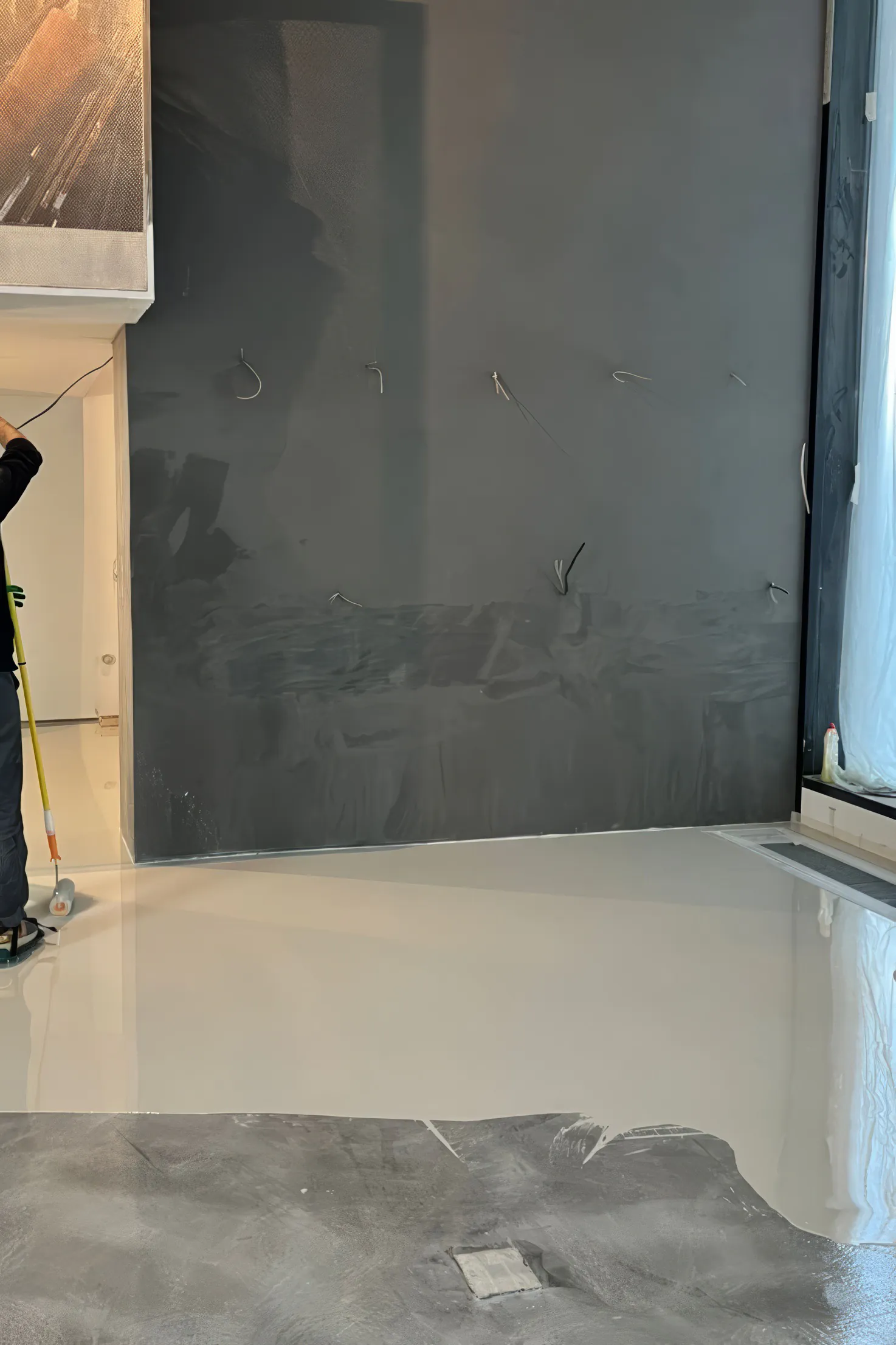 Человек в чёрной рубашке и тёмных брюках рядом со стеной с тёмно-серым участком.