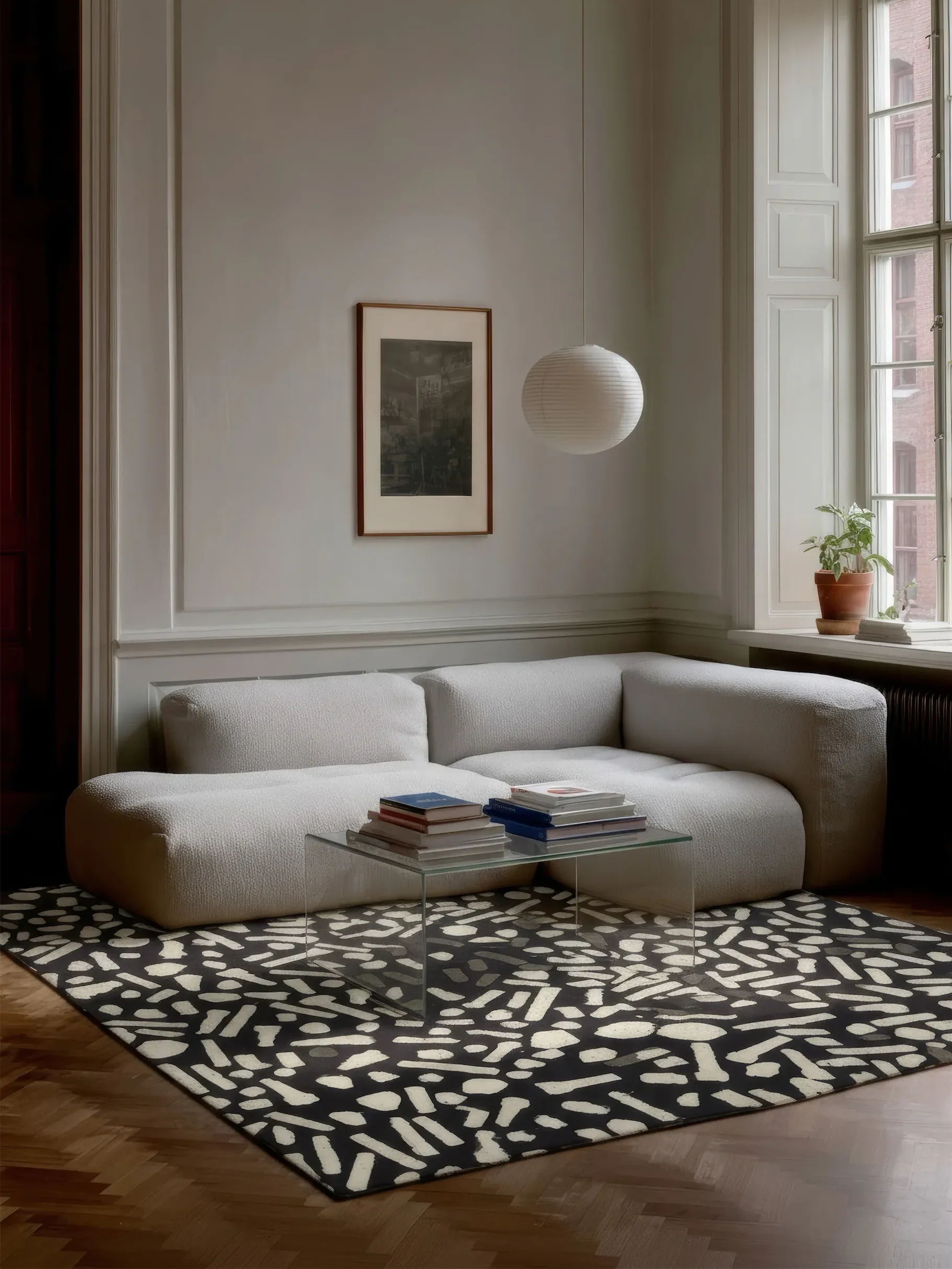 Светло-серый угловой диван на чёрно-белом ковре в комнате с белыми стенами.