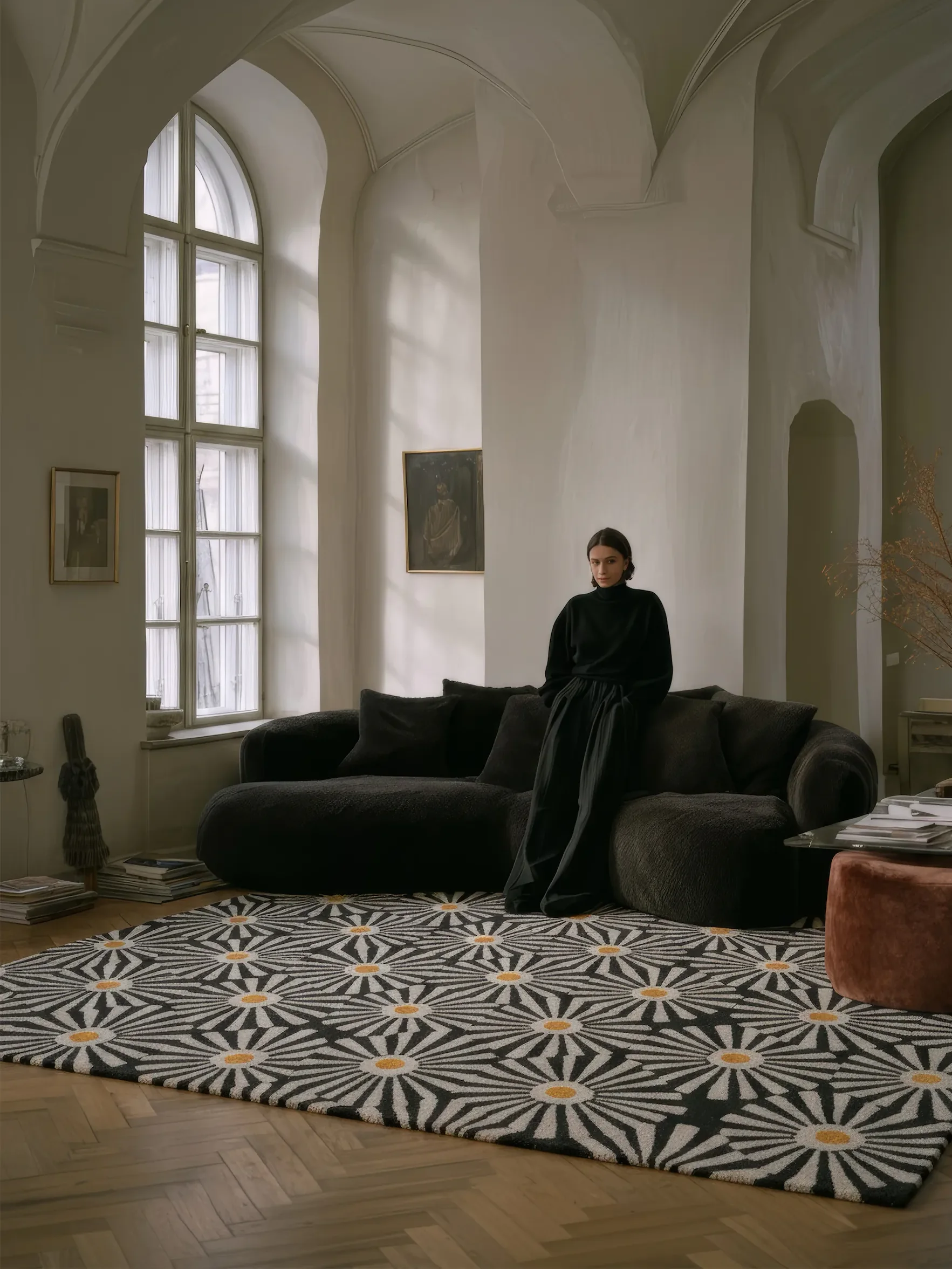 Женщина стоит на чёрно-белом ковре в комнате с белыми стенами и большим окном.