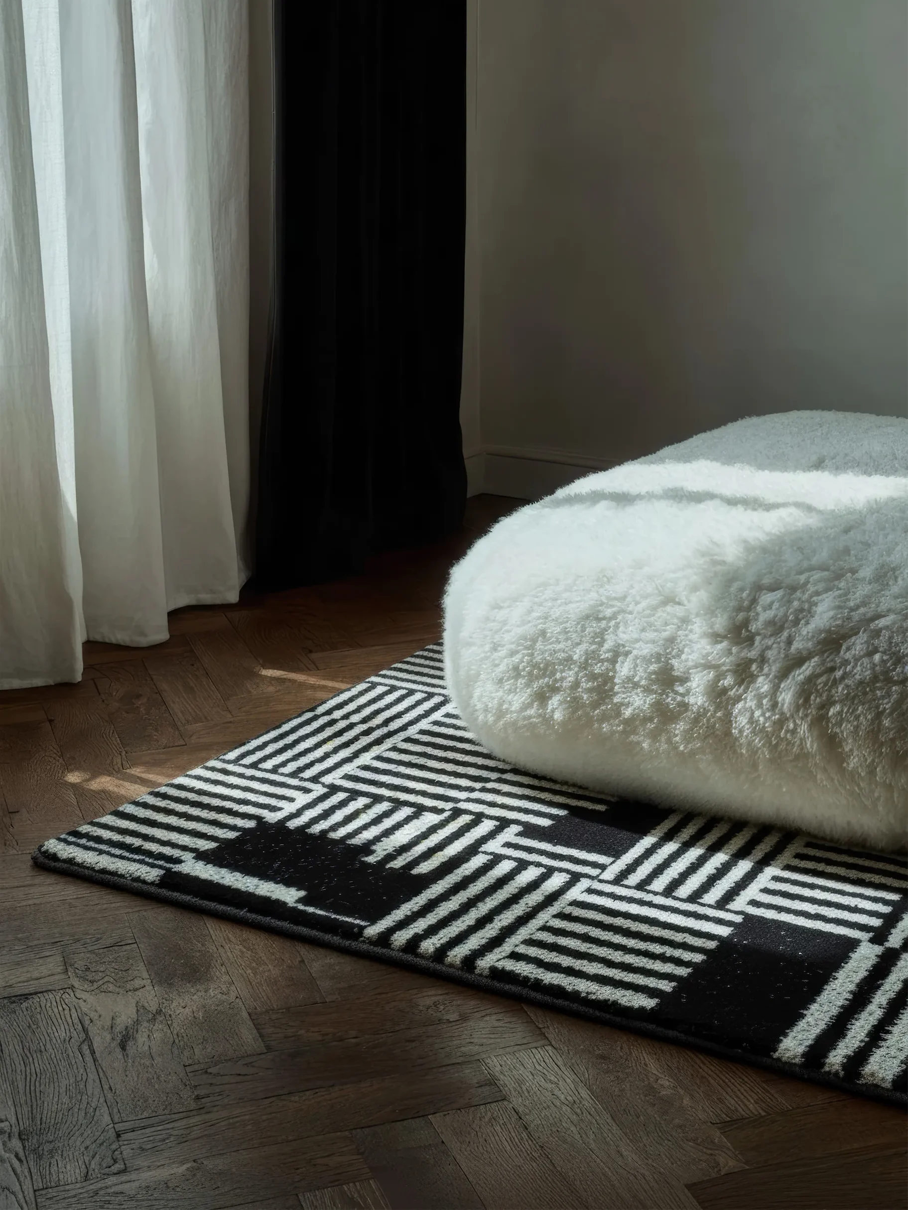 Белый пушистый предмет на чёрно-белом геометрическом ковре.