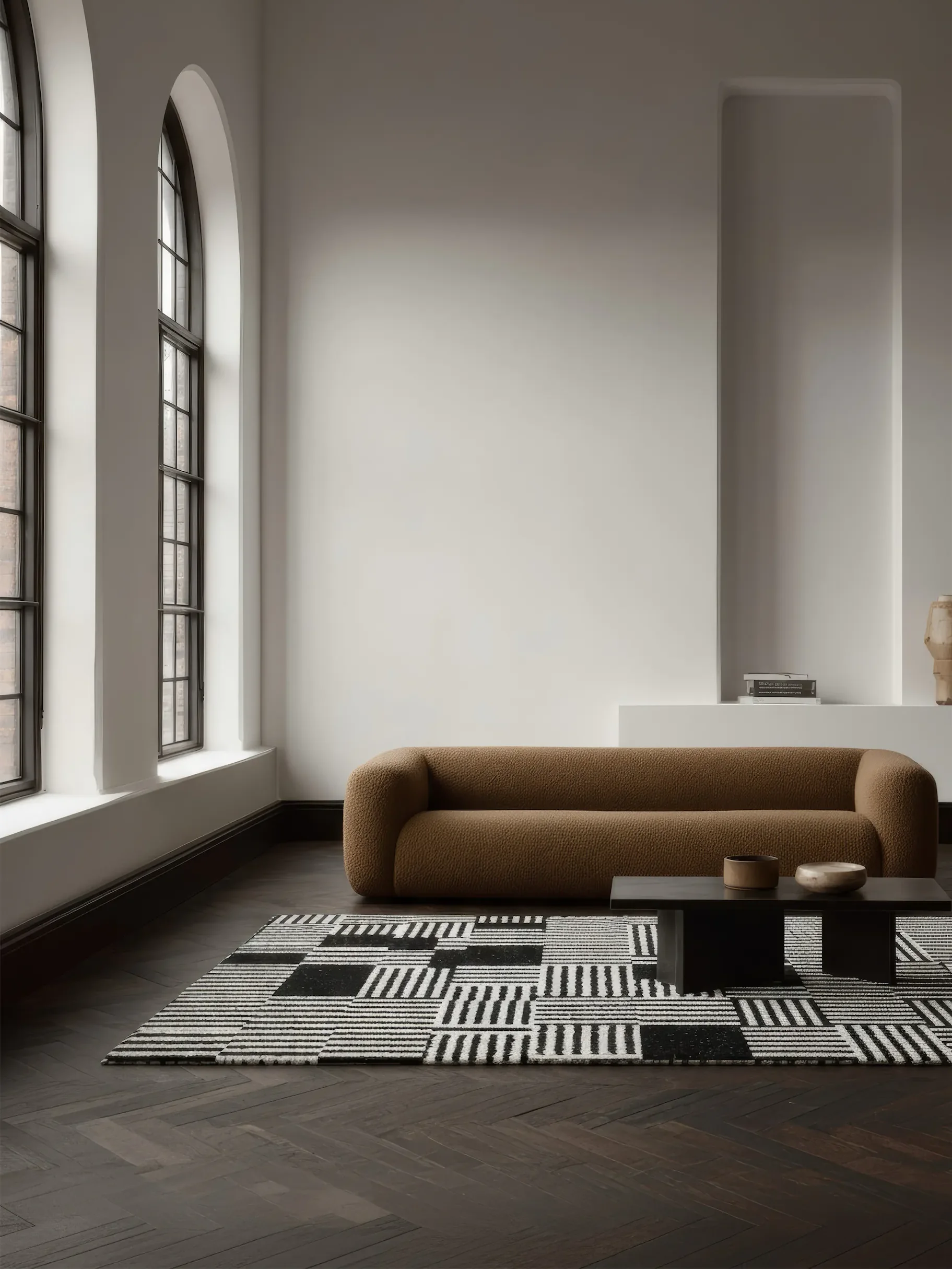 Минималистичная комната с бежевым диваном и кофейным столиком на геометрическом ковре. У стены камин и окно.