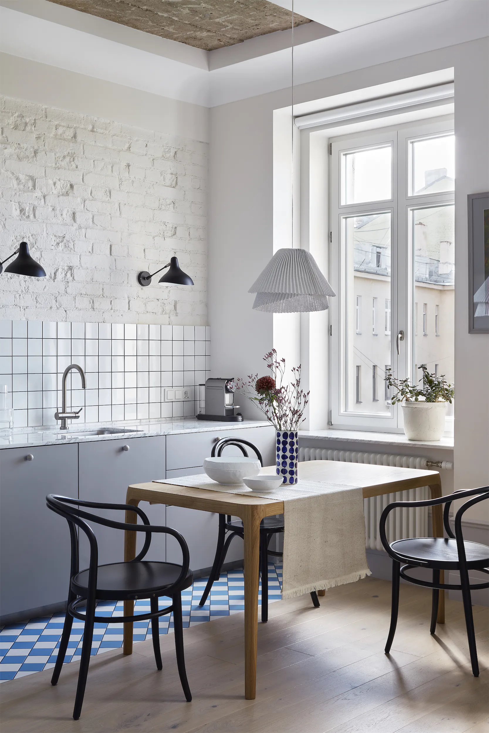 A minimalist kitchen with a small table and chairs, a window, and a sink in white and blue tones.