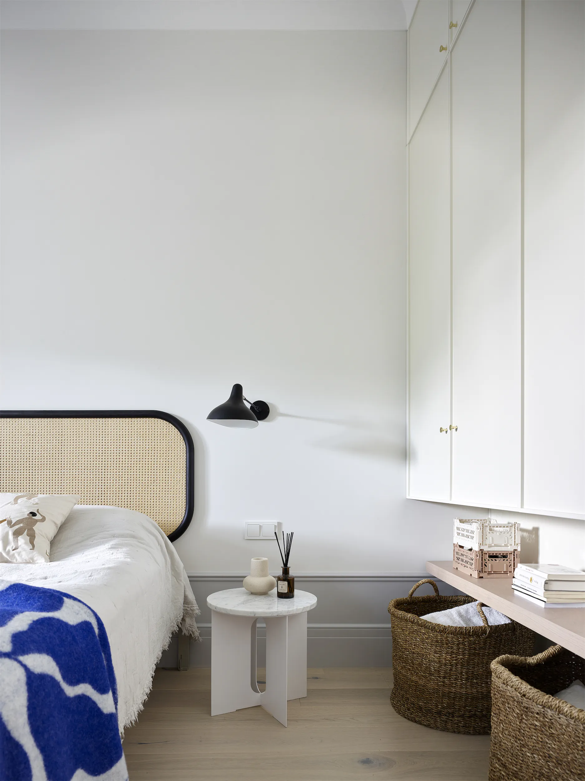 Белая стена с чёрным бра, кровать и небольшой столик.