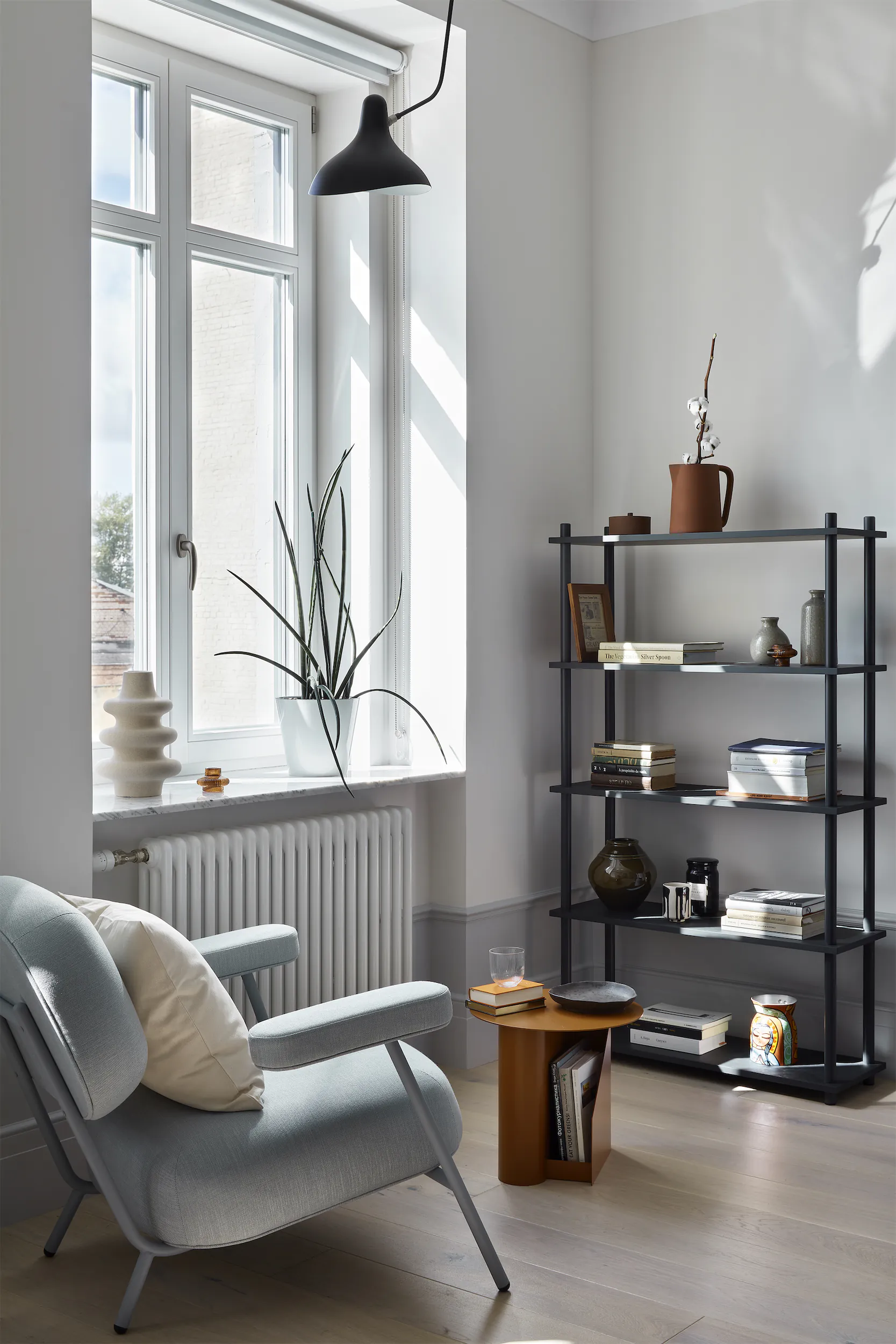 Минималистичная комната с серым креслом, деревянным журнальным столиком и чёрным стеллажом.
