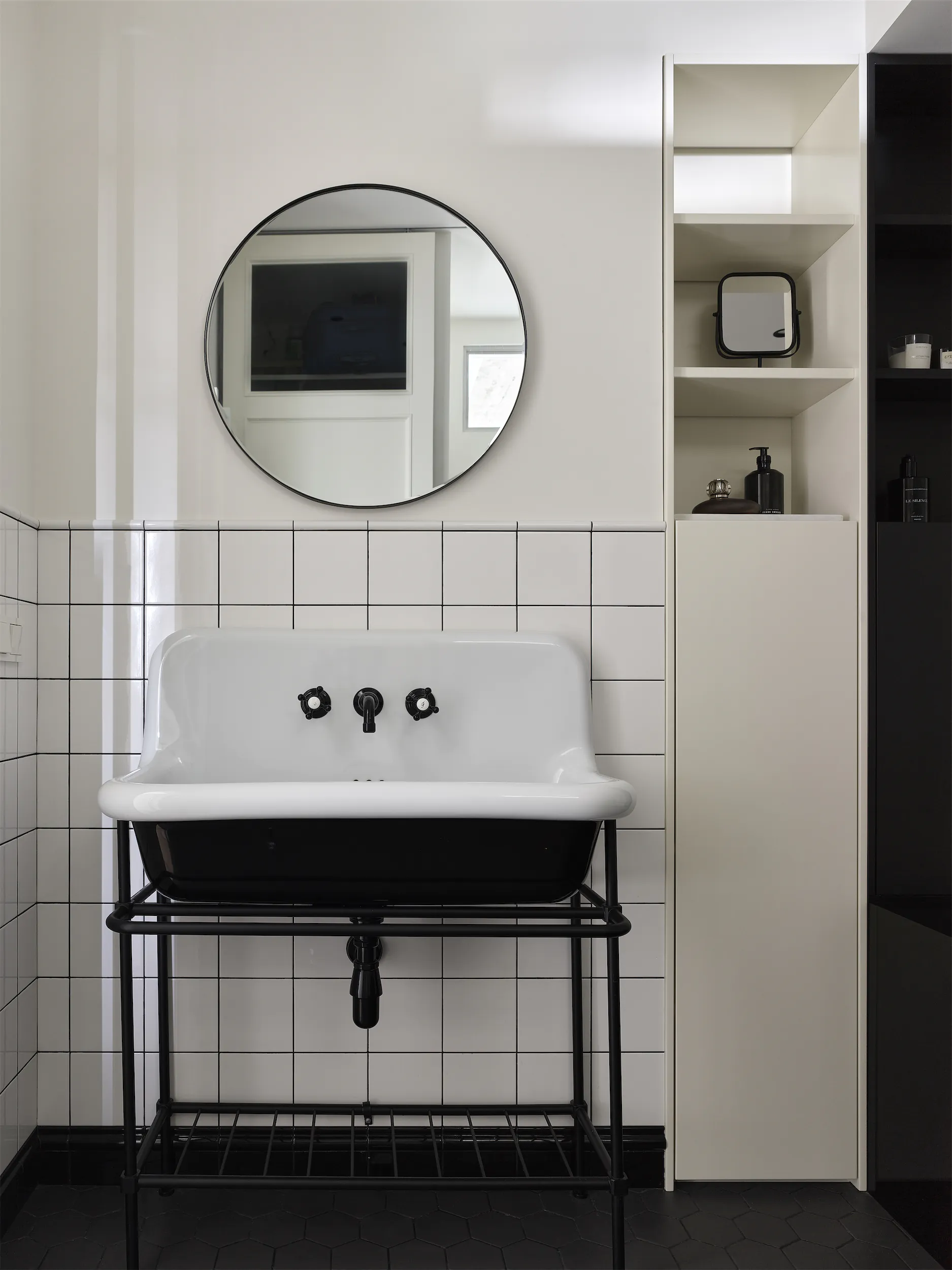 Белая раковина с чёрным смесителем под круглым зеркалом.