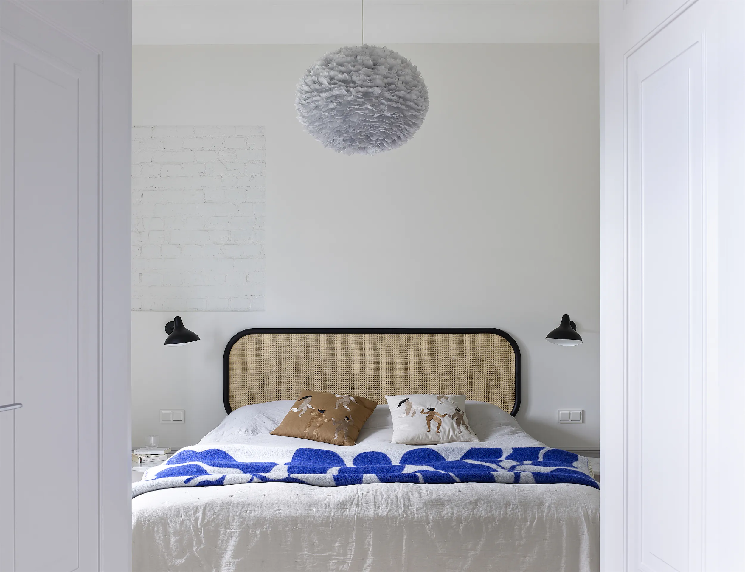 Белая спальня с кроватью. На кровати сине-белое покрывало, бежевая подушка и чёрно-белое изголовье.