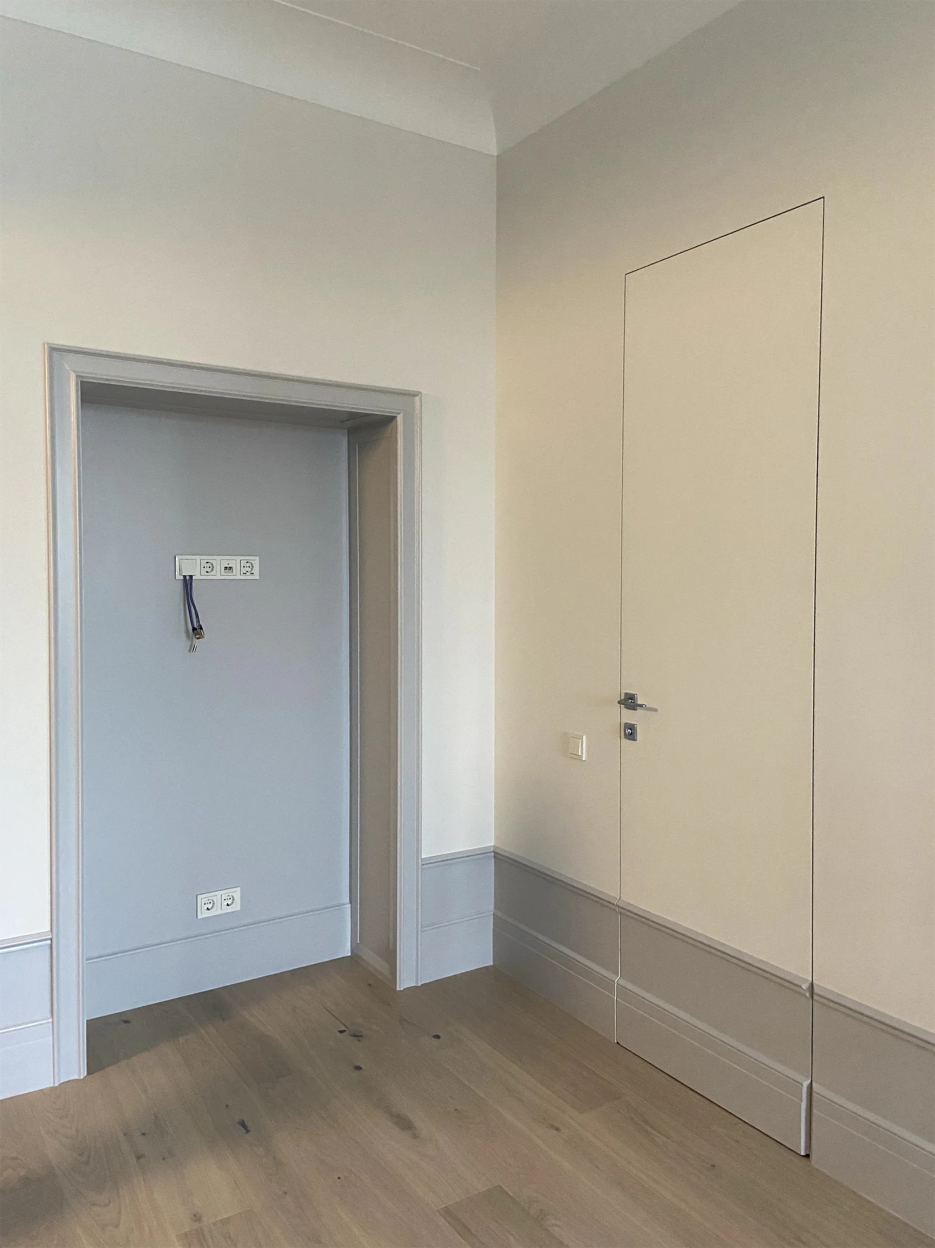 Дверной проём и выключатель на фоне белых стен и деревянного пола.