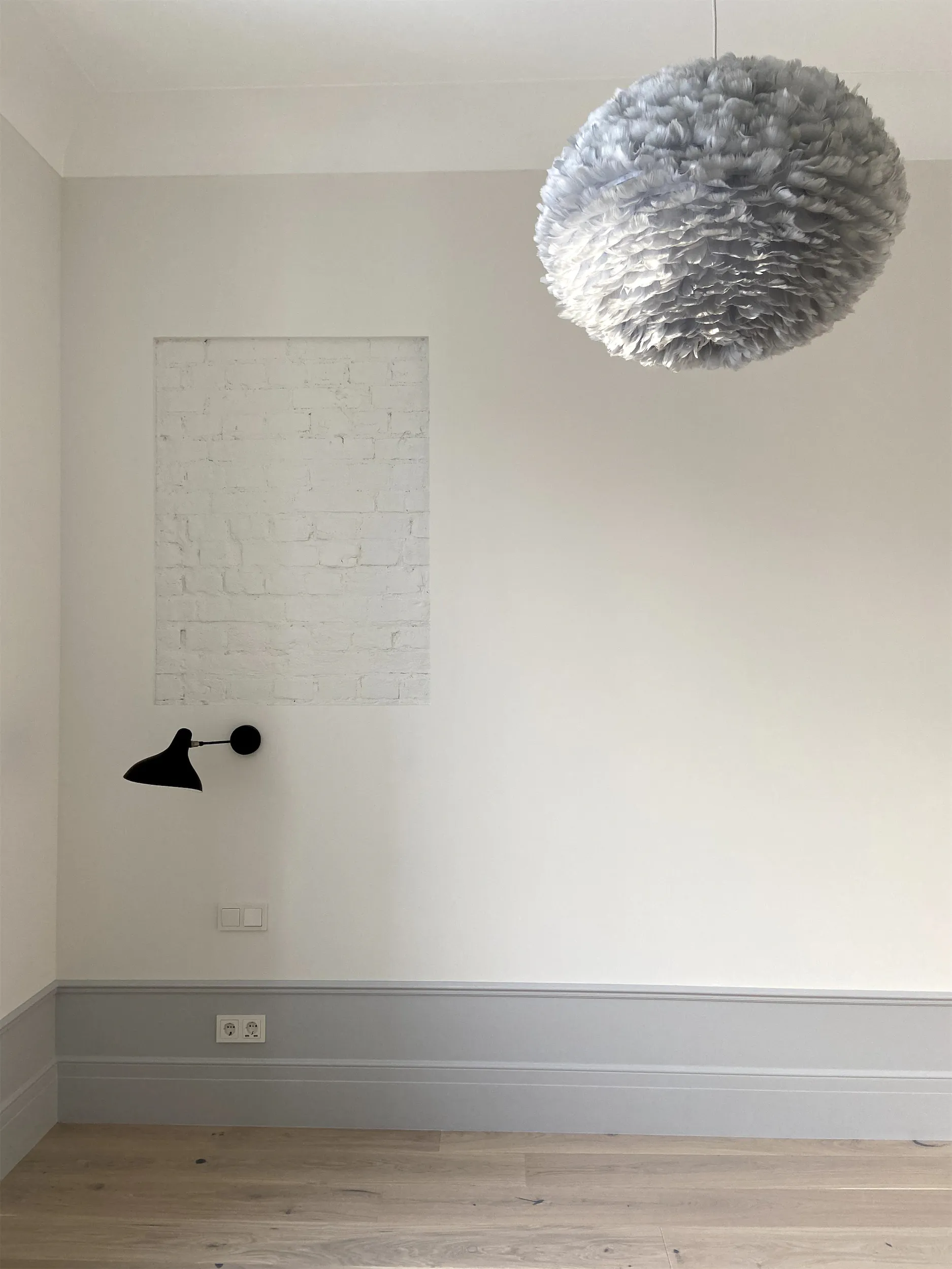 Белая комната с чёрным светильником и белым потолком.