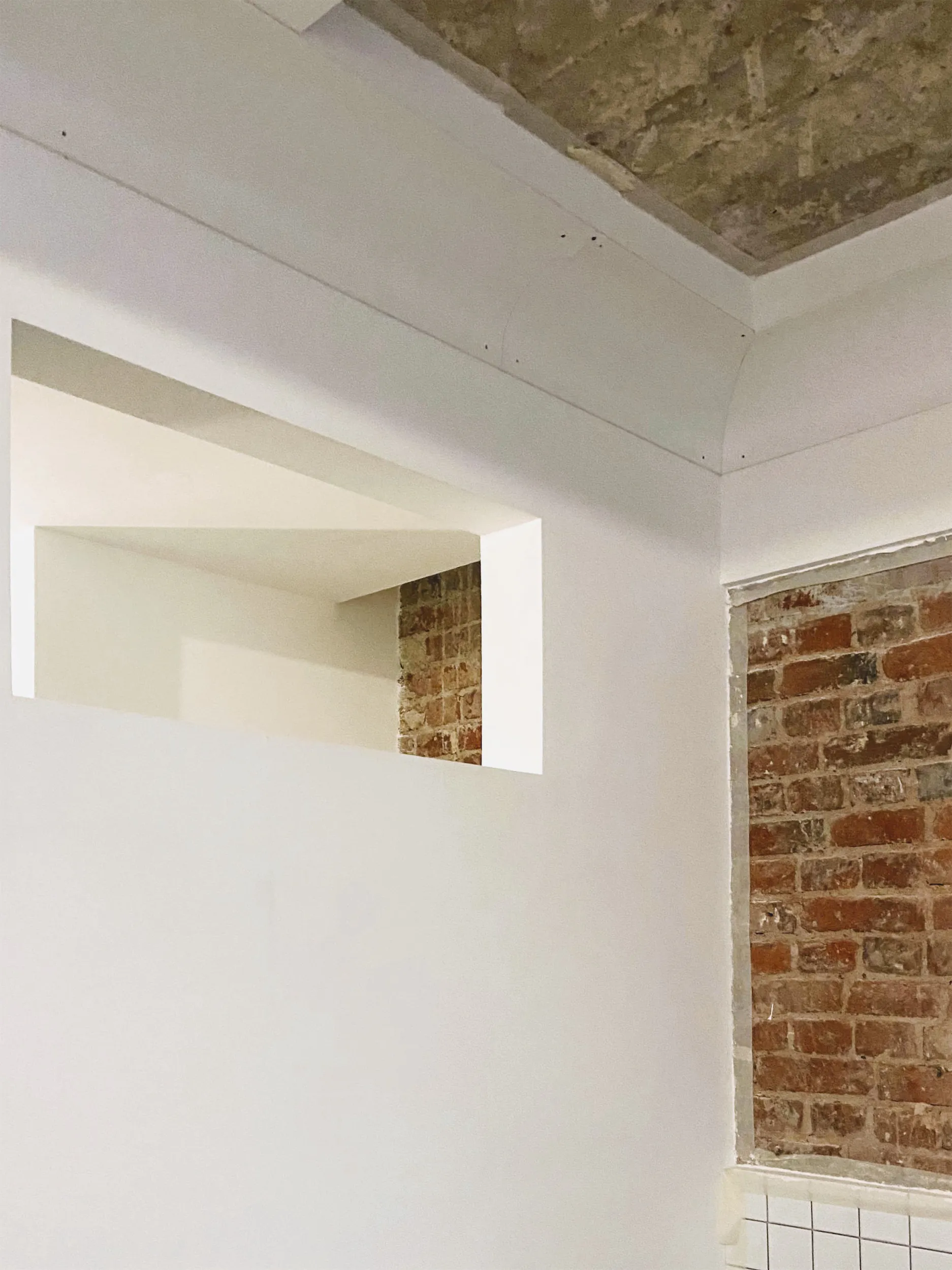 Белая стена с кирпичным откосом окна и углублённым верхним углом.