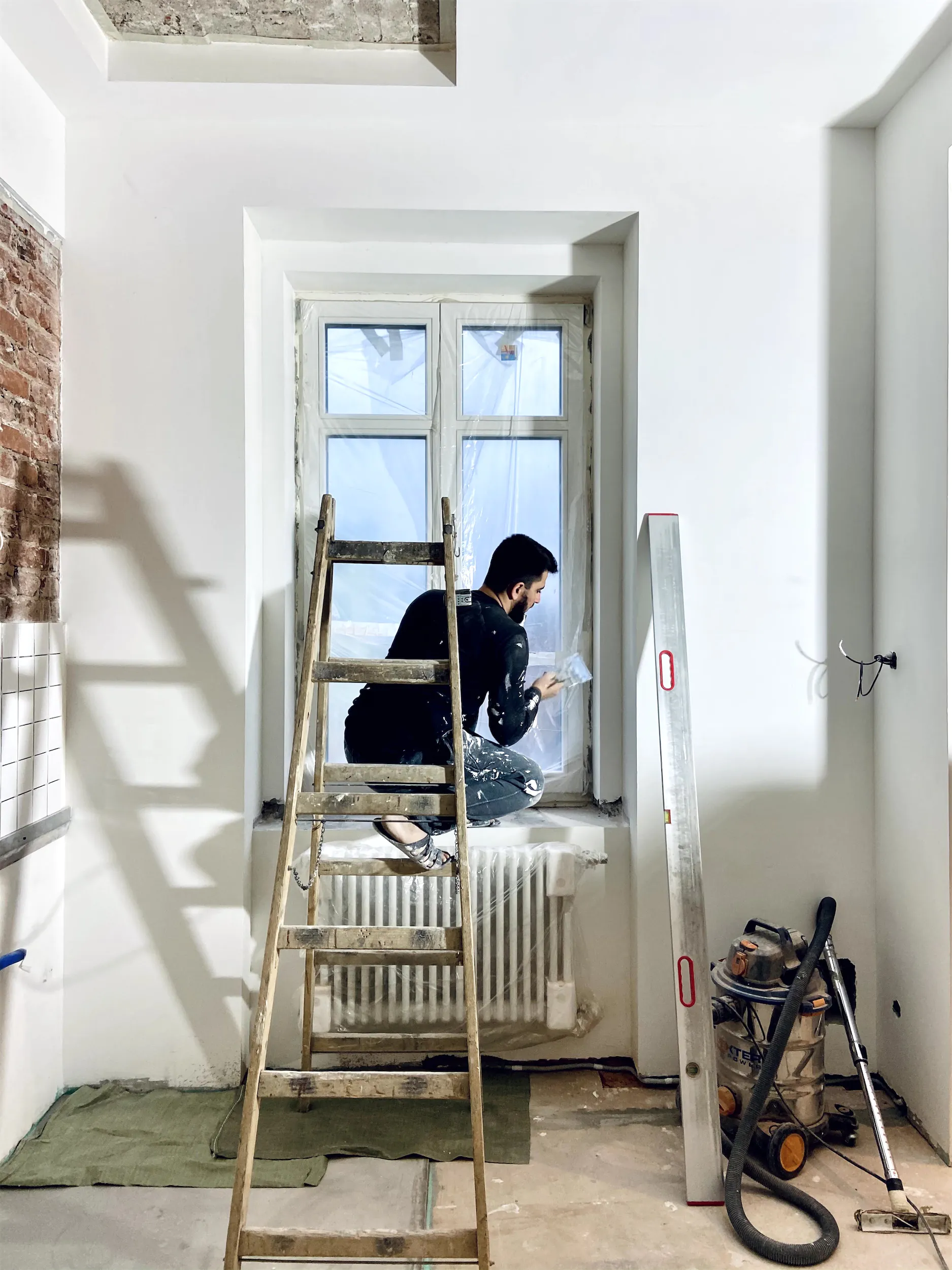 Мужчина сидит на подоконнике в комнате с белыми стенами и лестницей.