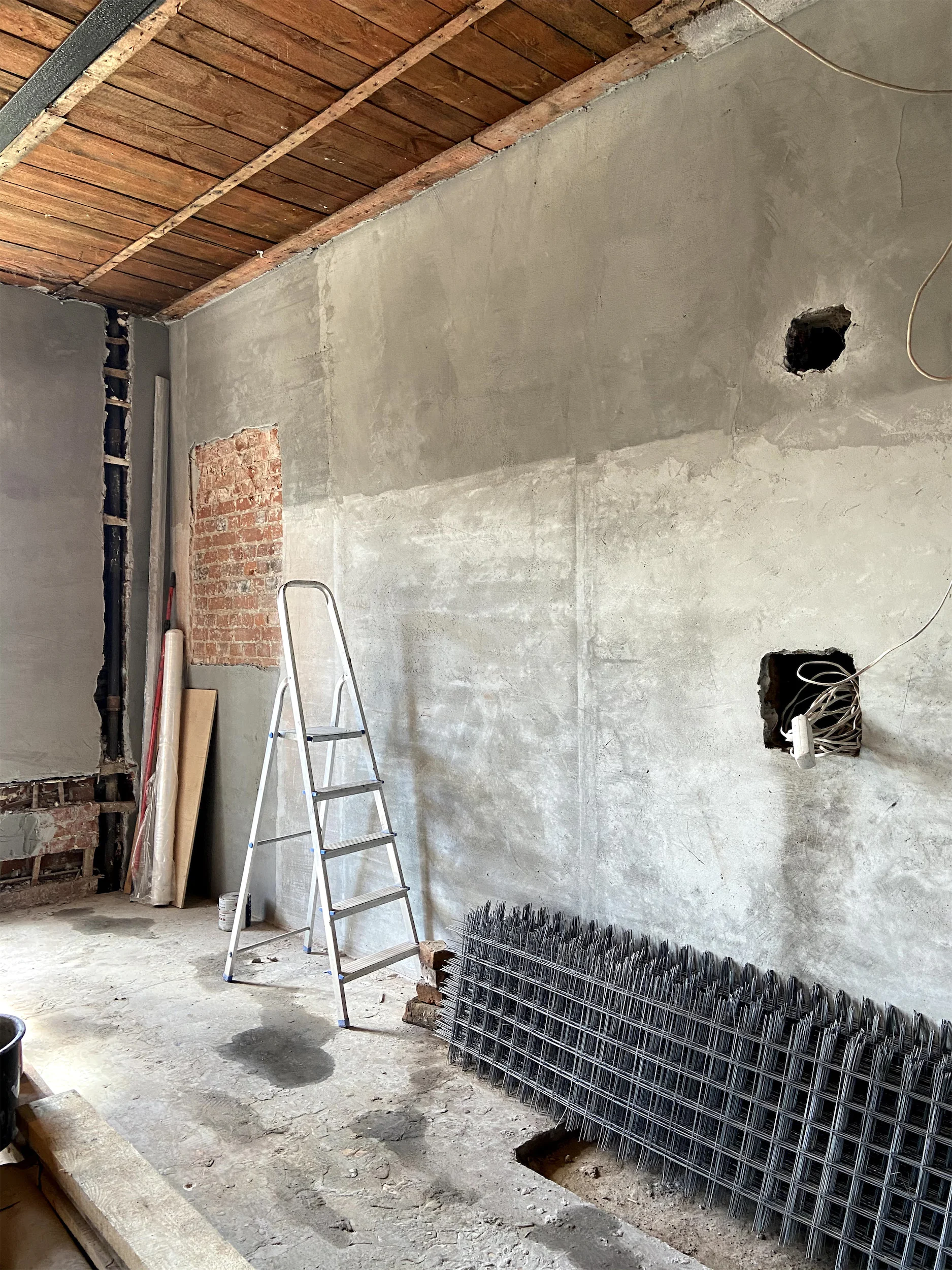 Комната с открытой кирпичной кладкой, лестницей и металлической решёткой на полу.