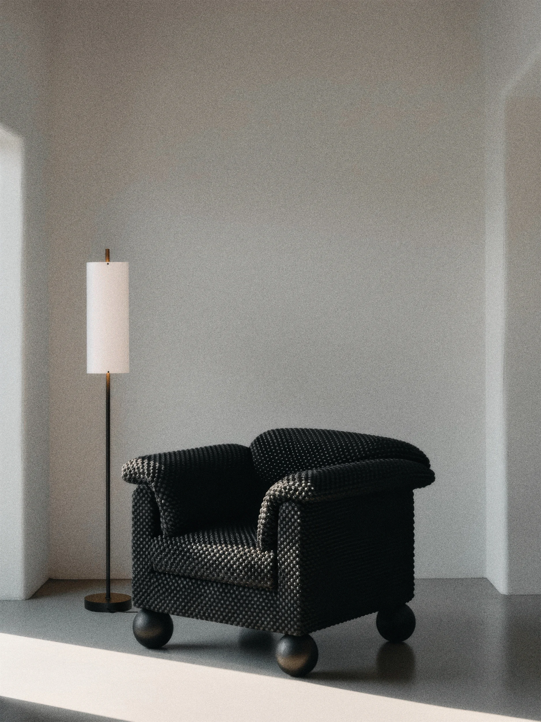 A black armchair on a dark gray floor in a minimalist white room with a floor lamp.