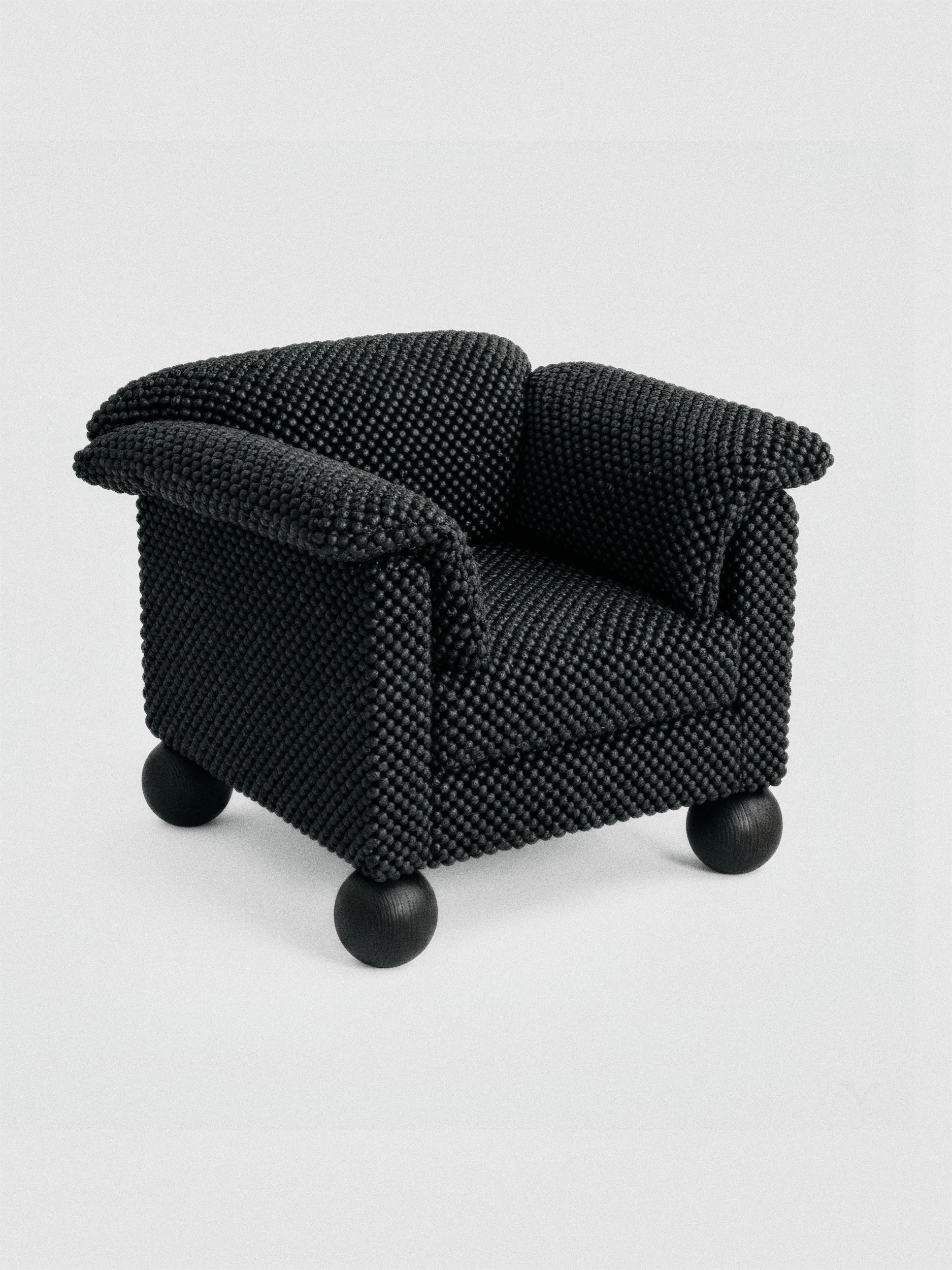 Чёрное кресло с текстурной обивкой и небольшими круглыми ножками на светло-сером фоне.