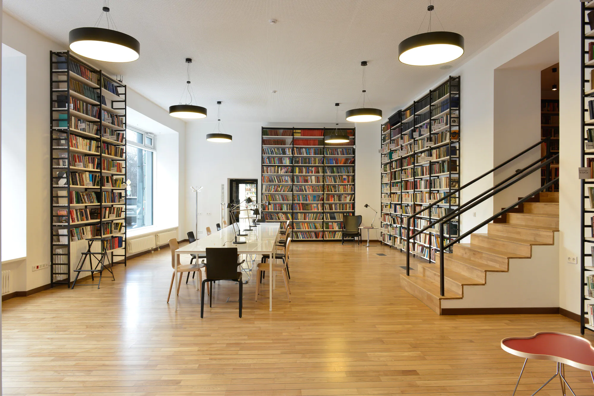 A room with a staircase, a bookshelf wall, and a table with chairs.