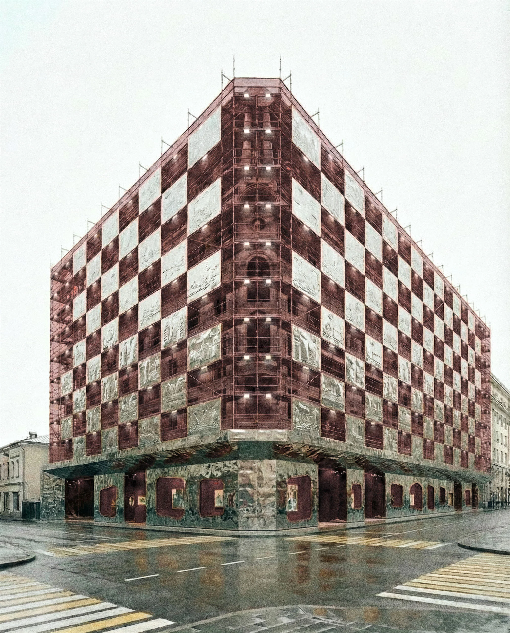 Многоэтажное здание с клетчатым фасадом над магазином на уровне улицы. Мокрый тротуар.