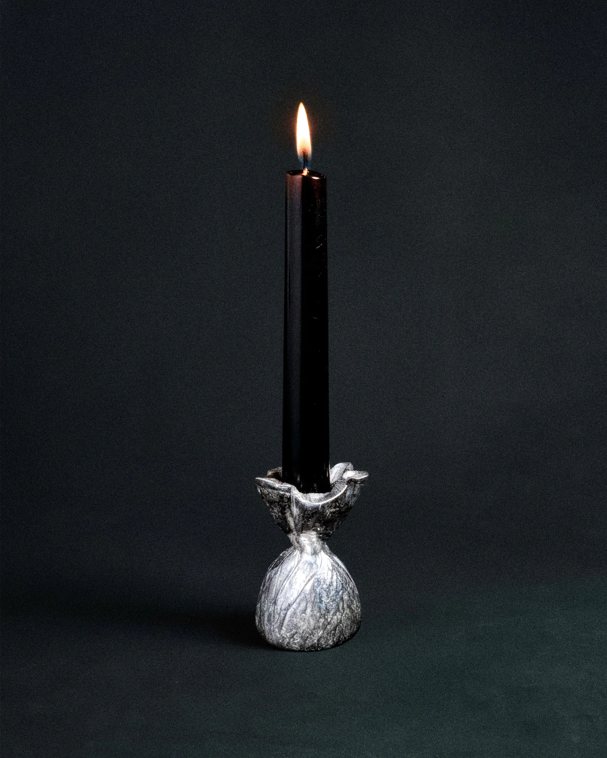 Чёрная свеча в белом керамическом подсвечнике с птичьим орнаментом на тёмном фоне.