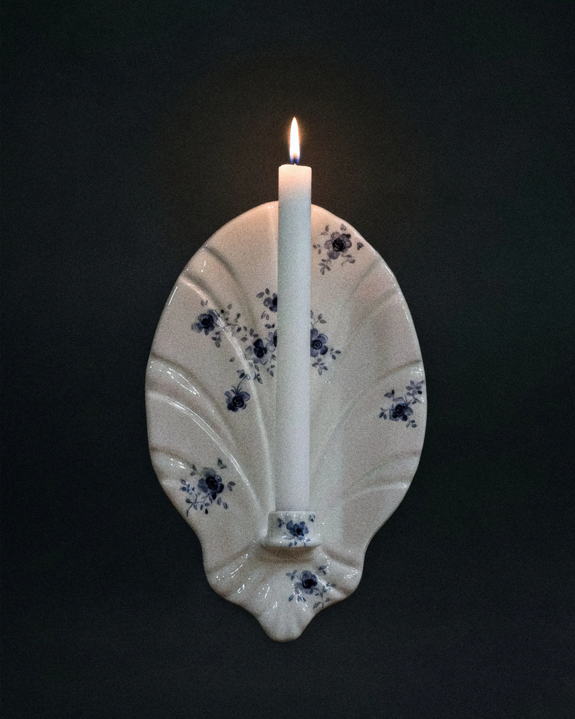 Белая свеча с синим цветочным рисунком на декоративной подставке в форме ракушки.