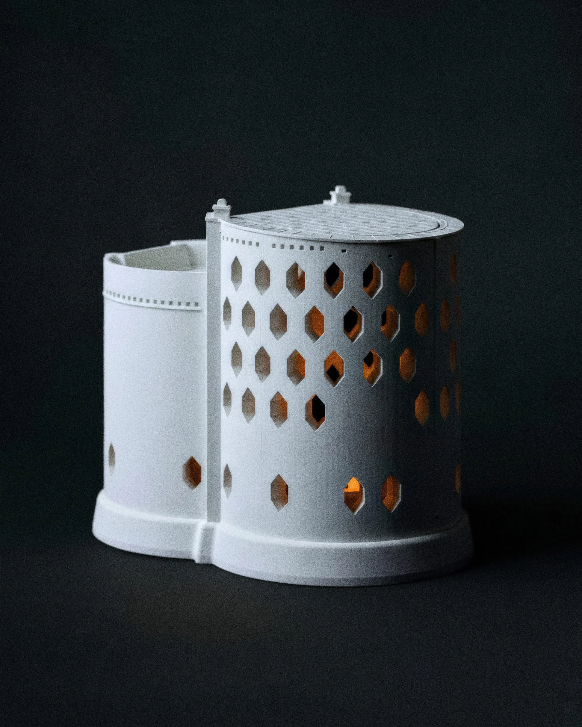 Белый цилиндрический подсвечник с перфорацией на чёрном фоне.