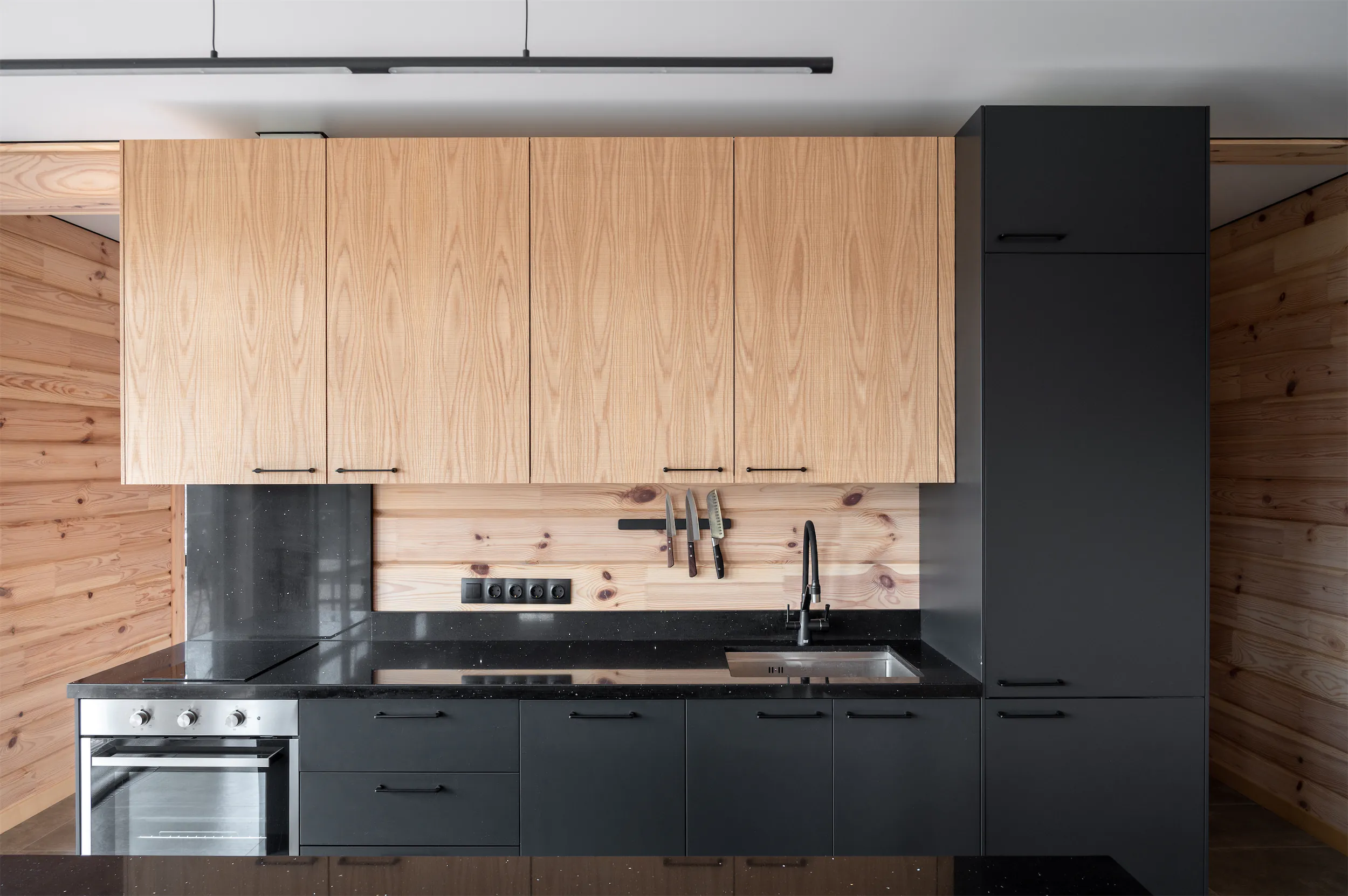 Кухня с тёмно-серыми шкафами и столешницами, светлыми деревянными акцентами и духовкой из нержавеющей стали.