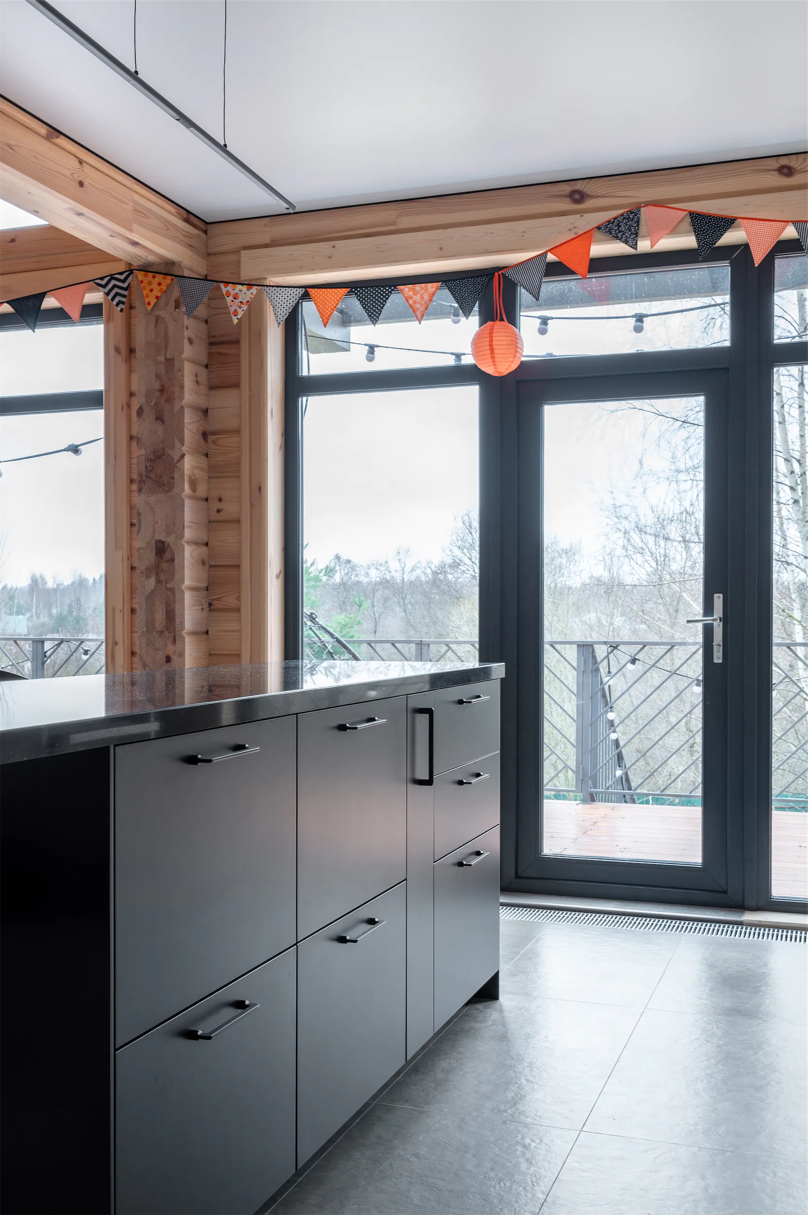 Кухня с серыми шкафами, чёрной столешницей и стеклянной раздвижной дверью на террасу.