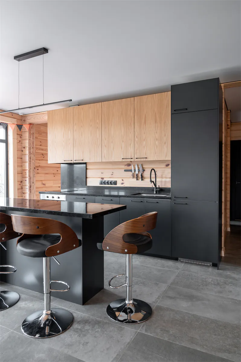 Современная кухня с гладкой чёрной столешницей, деревянными табуретами и минималистичным дизайном.