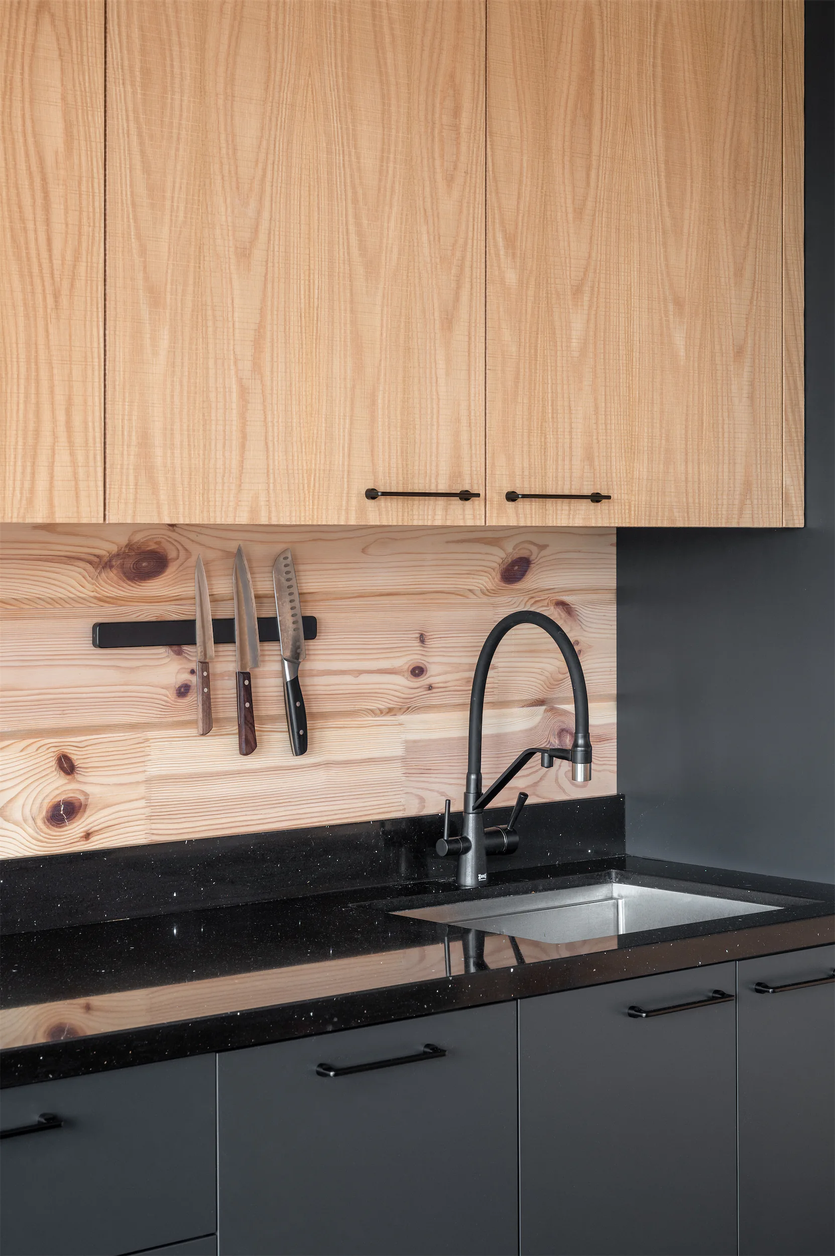 Кухня с чёрной раковиной, смесителем и столешницей, деревянные шкафы.