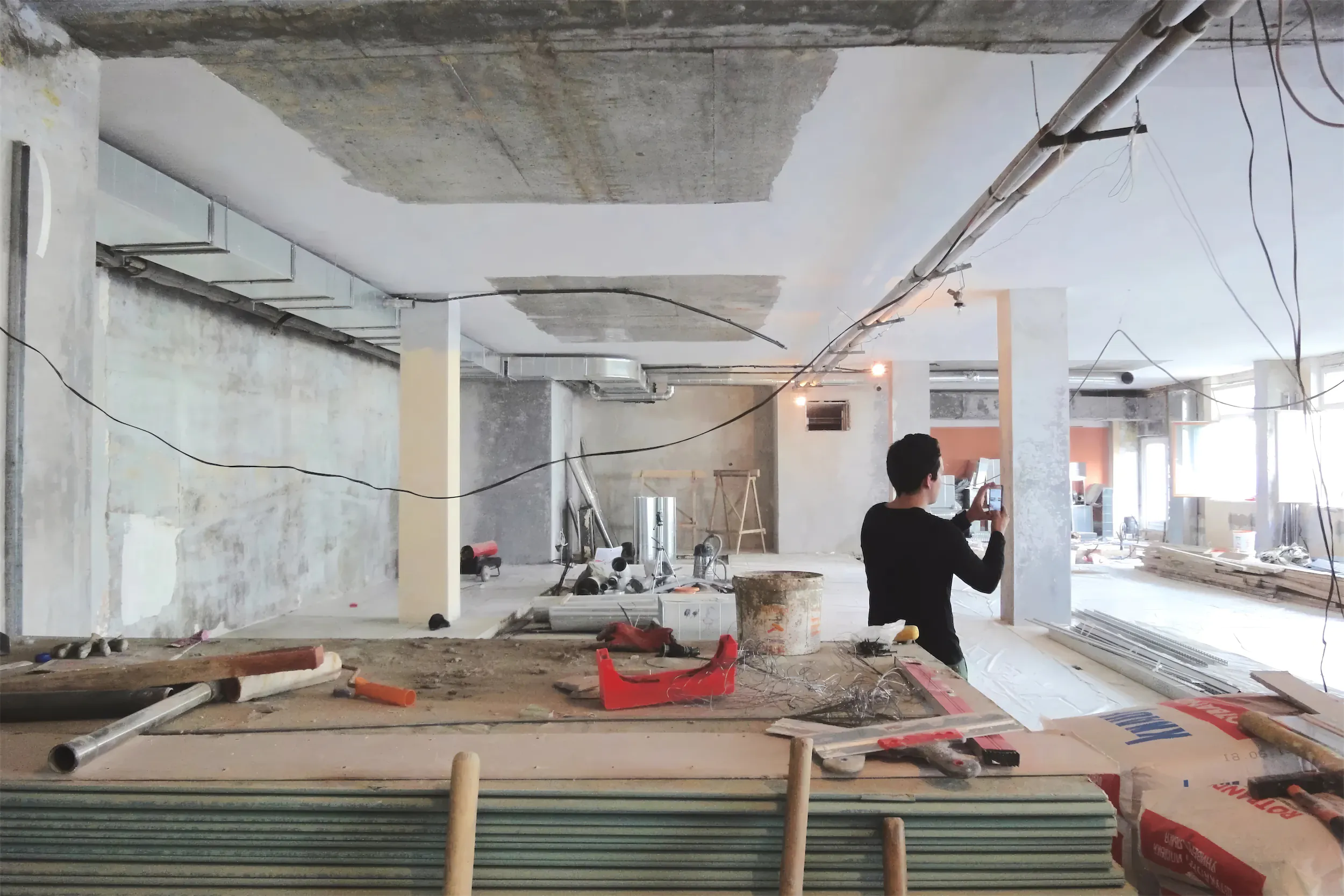 Человек в чёрной рубашке среди строительных материалов в незавершённом помещении.