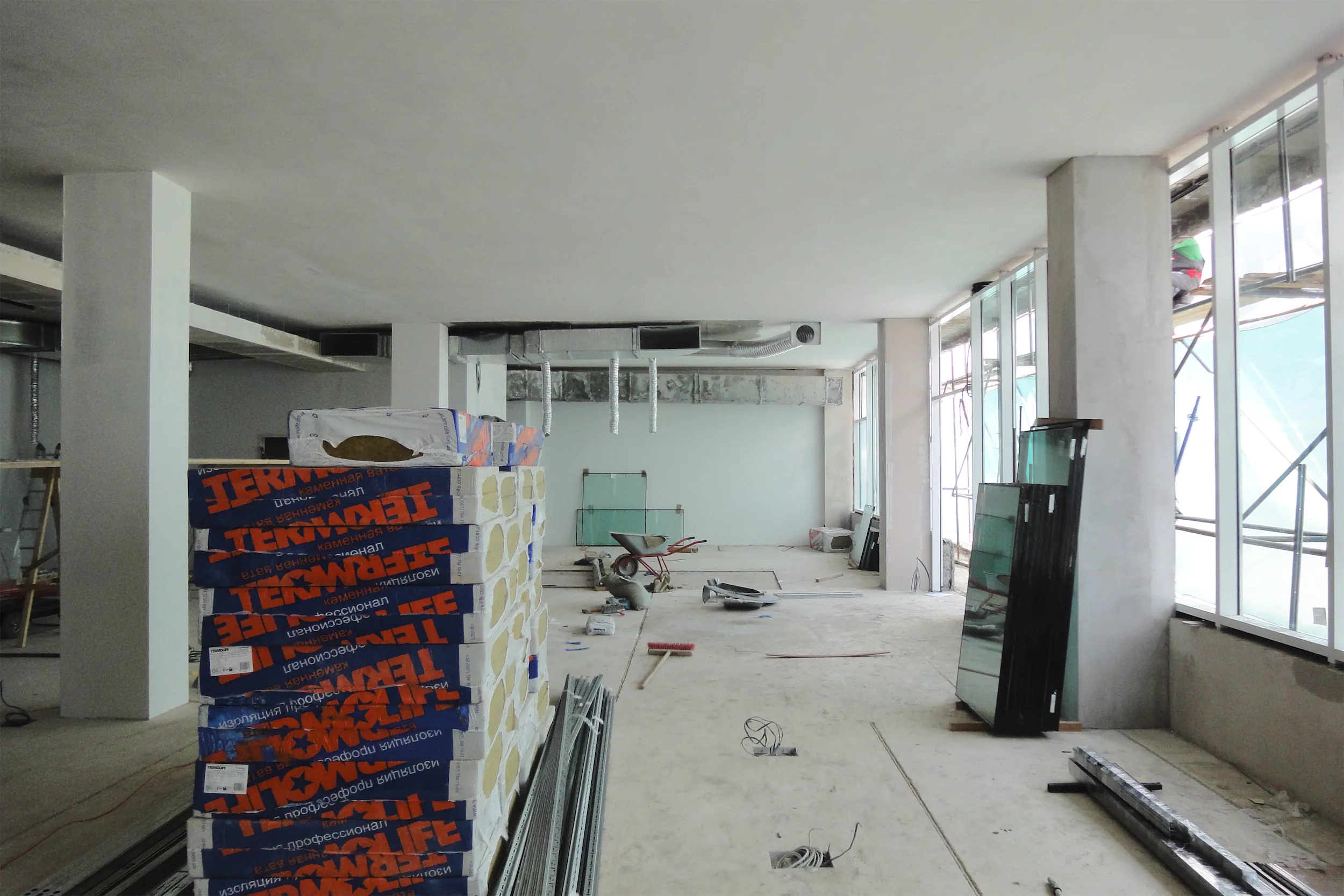 Большое помещение в процессе ремонта. На полу стопки коробок и разбросанный инструмент.