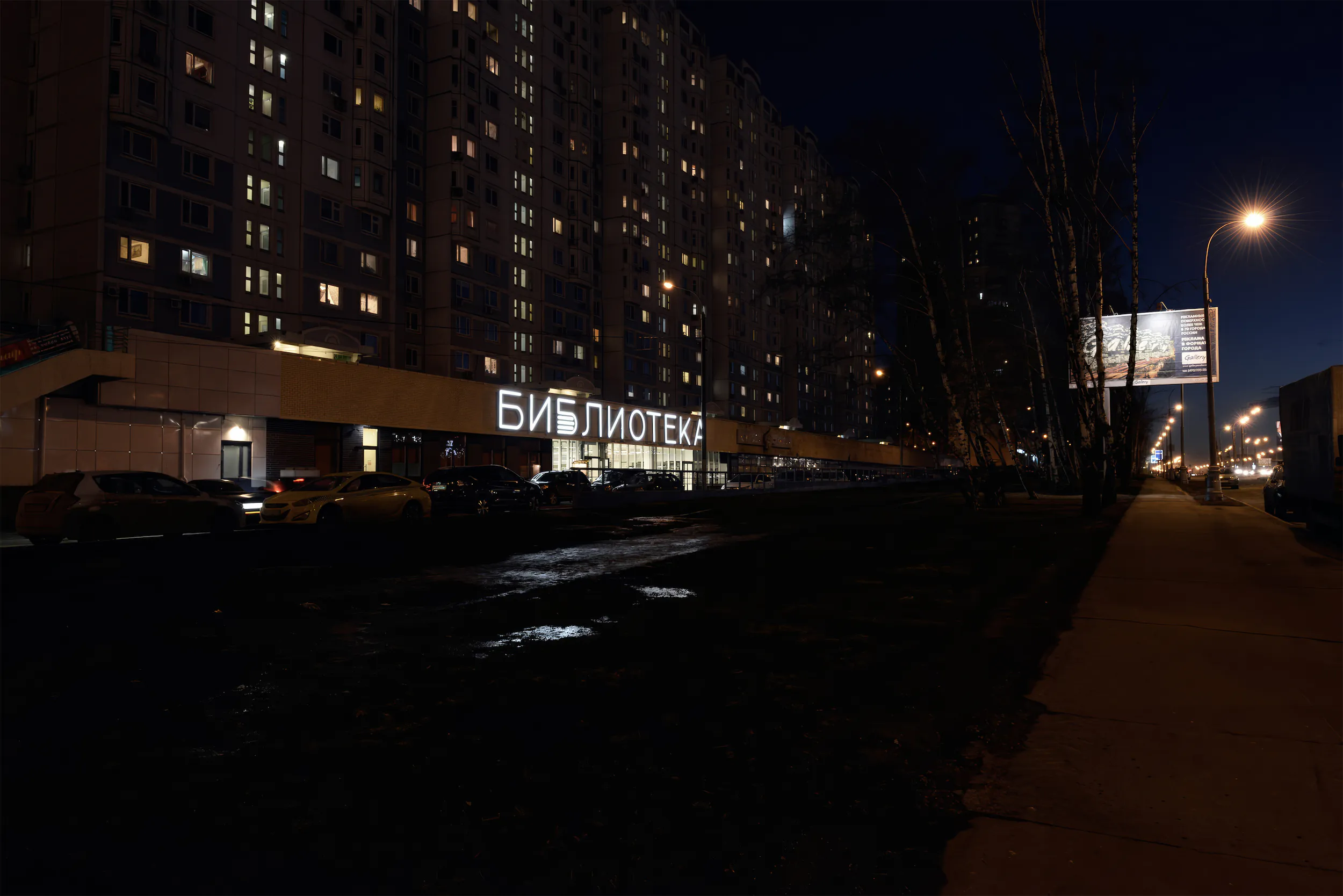 Ночная городская панорама с зданием и крупной светящейся вывеской.