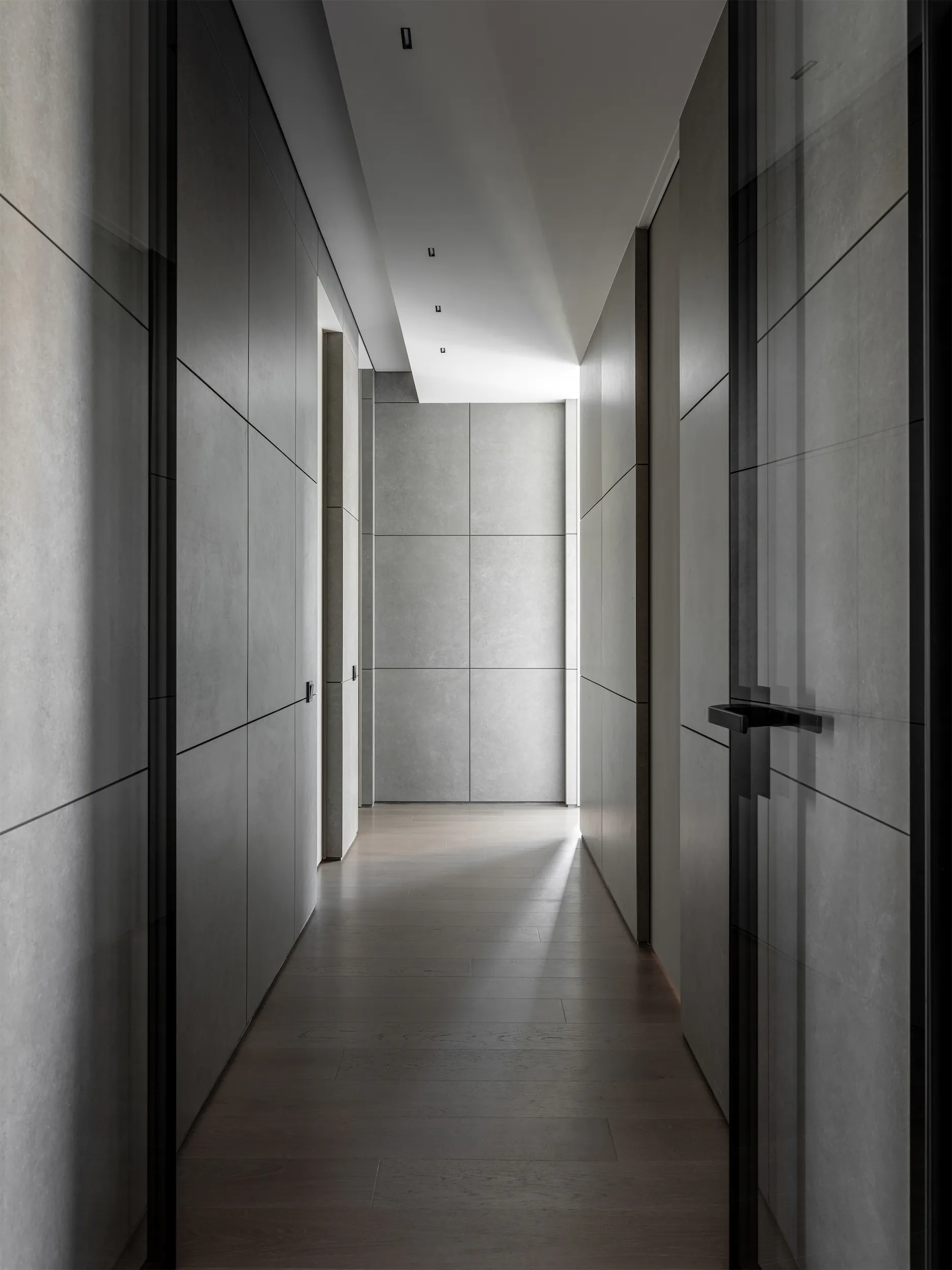 A narrow hallway with white walls and a door with a black handle at the end.
