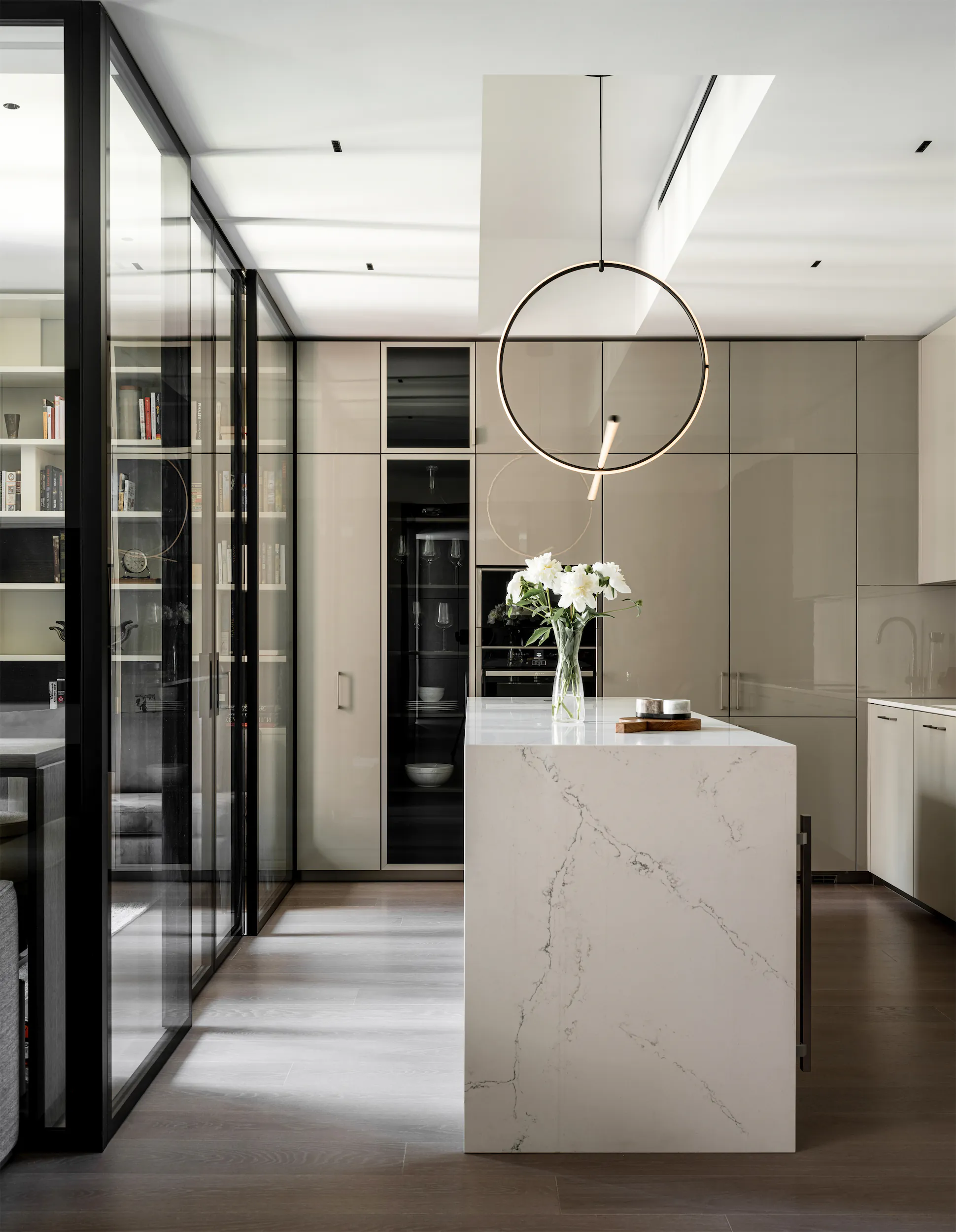 Современная кухня с белым мраморным островом, круглым светильником и вазой с цветами.