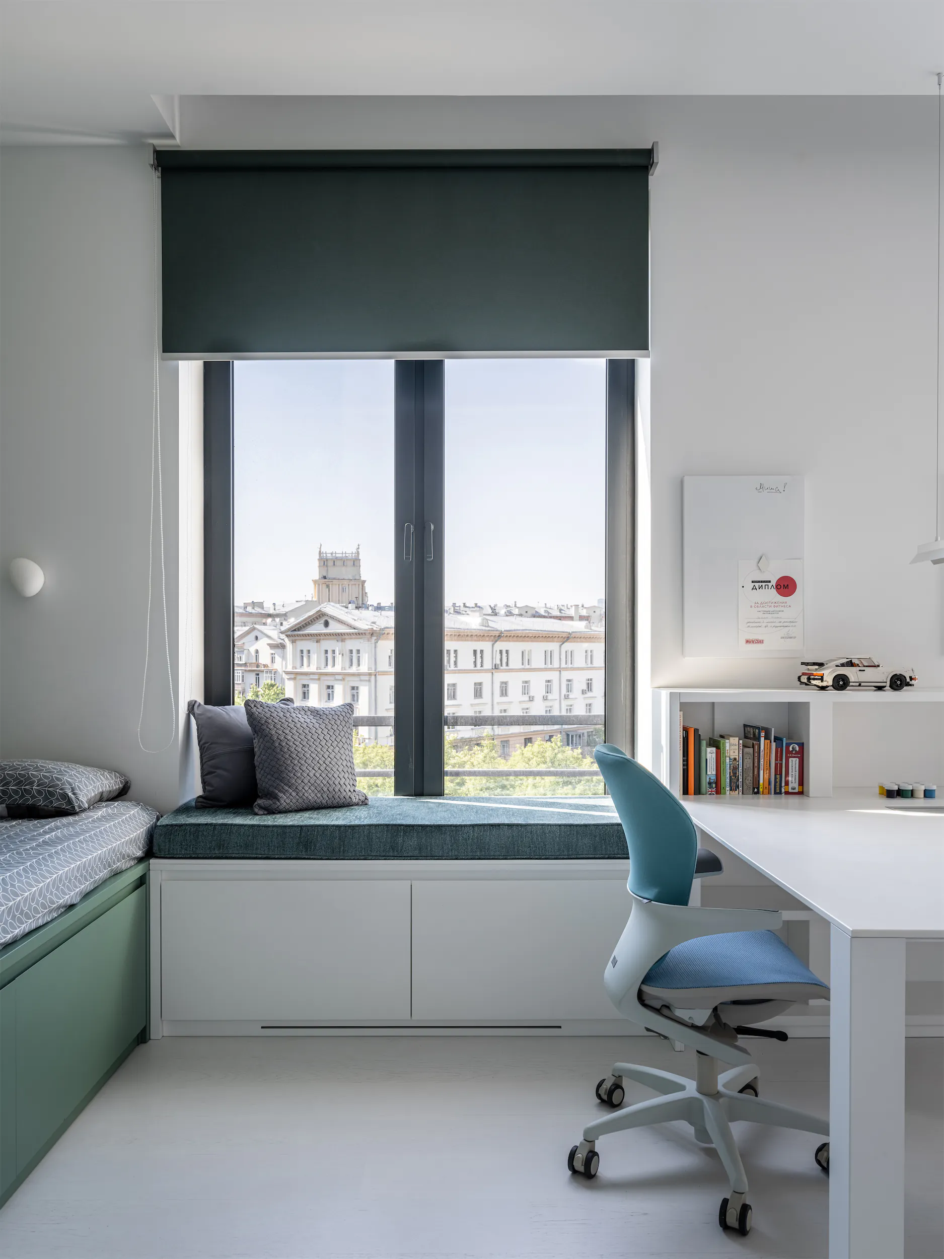 Комната с диванчиком у окна, столом и стулом в бело-зелёной гамме.