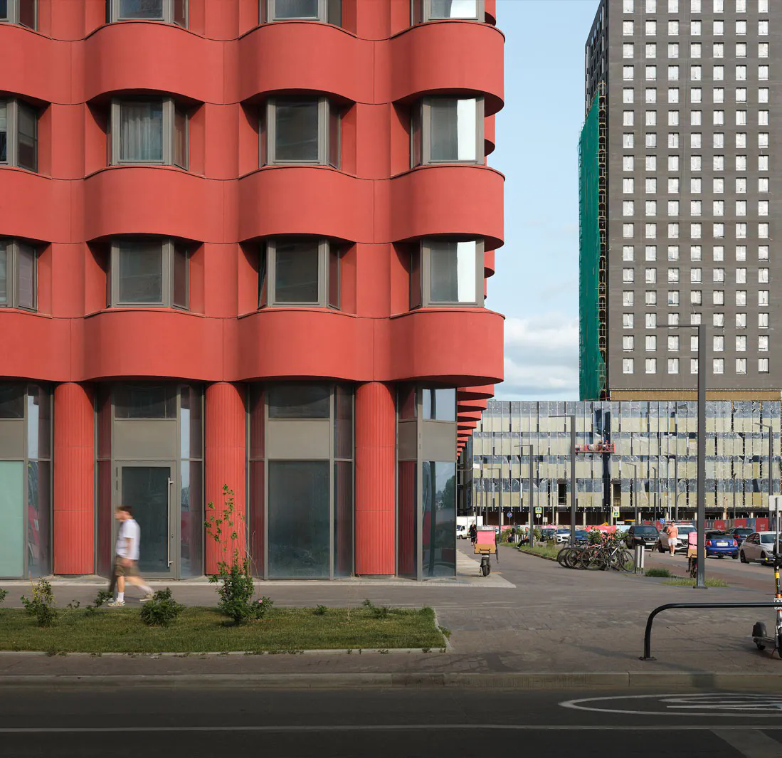 A modern red building with a curved facade and many windows on a street corner.